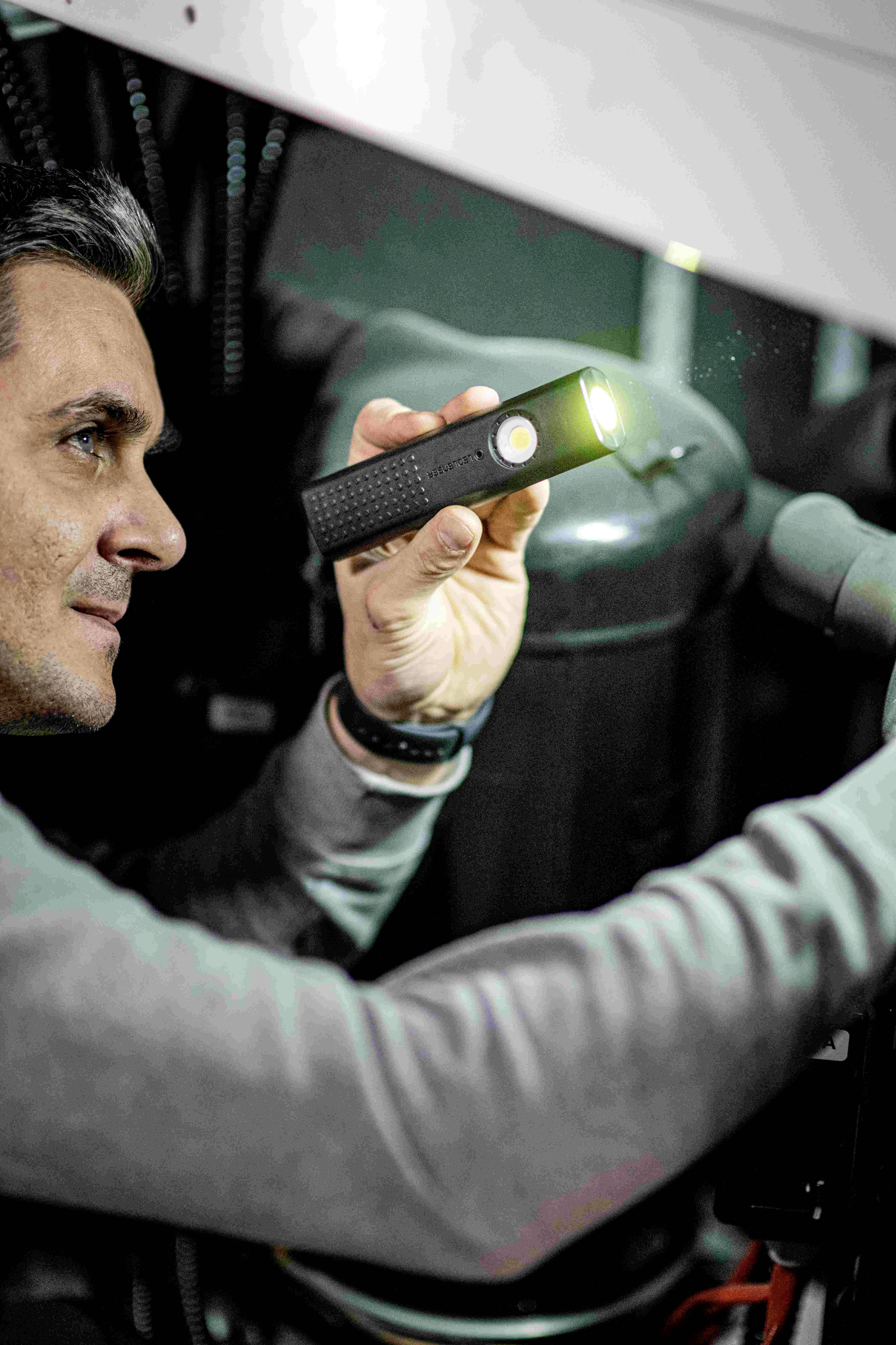 Een persoon inspecteert met een zaklamp de technische componenten van een machine in een werkplaatsomgeving.