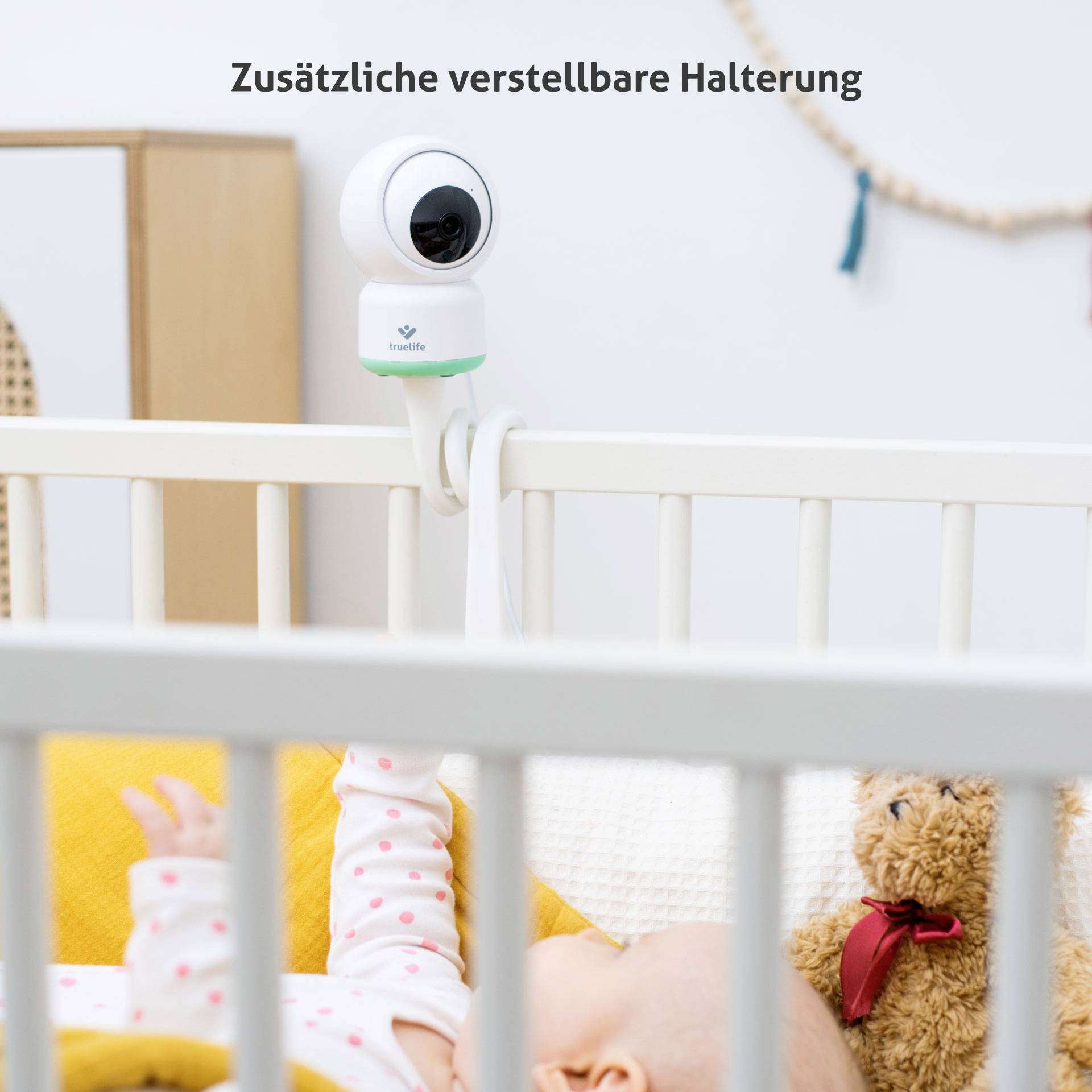 'Babyfoon-camera met verstelbare houder gemonteerd aan een kinderbed. Slapende baby op de voorgrond.'