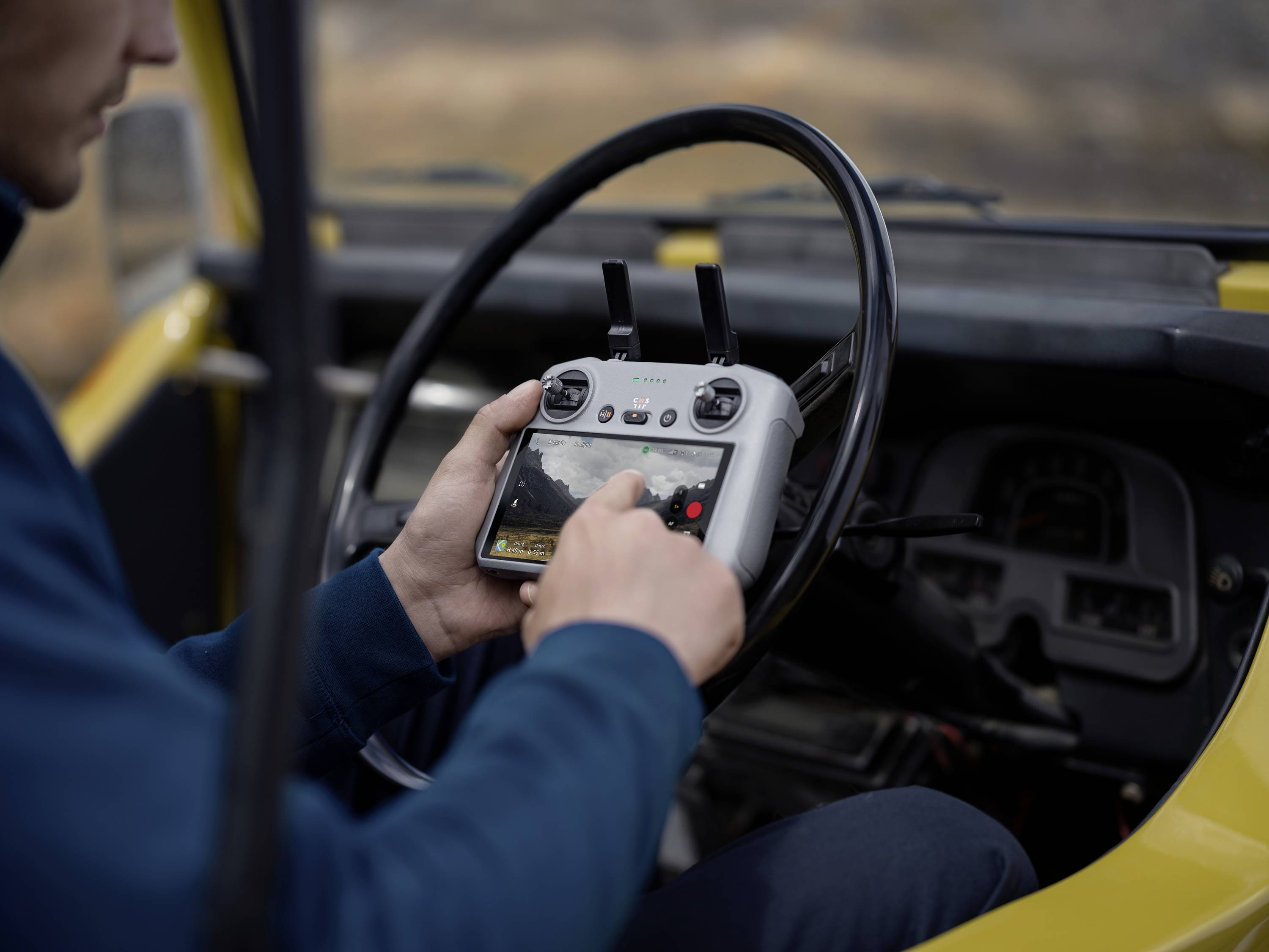 Een persoon in een blauw shirt bedient een afstandsbediening in een geel voertuig, mogelijk een drone aan het besturen.