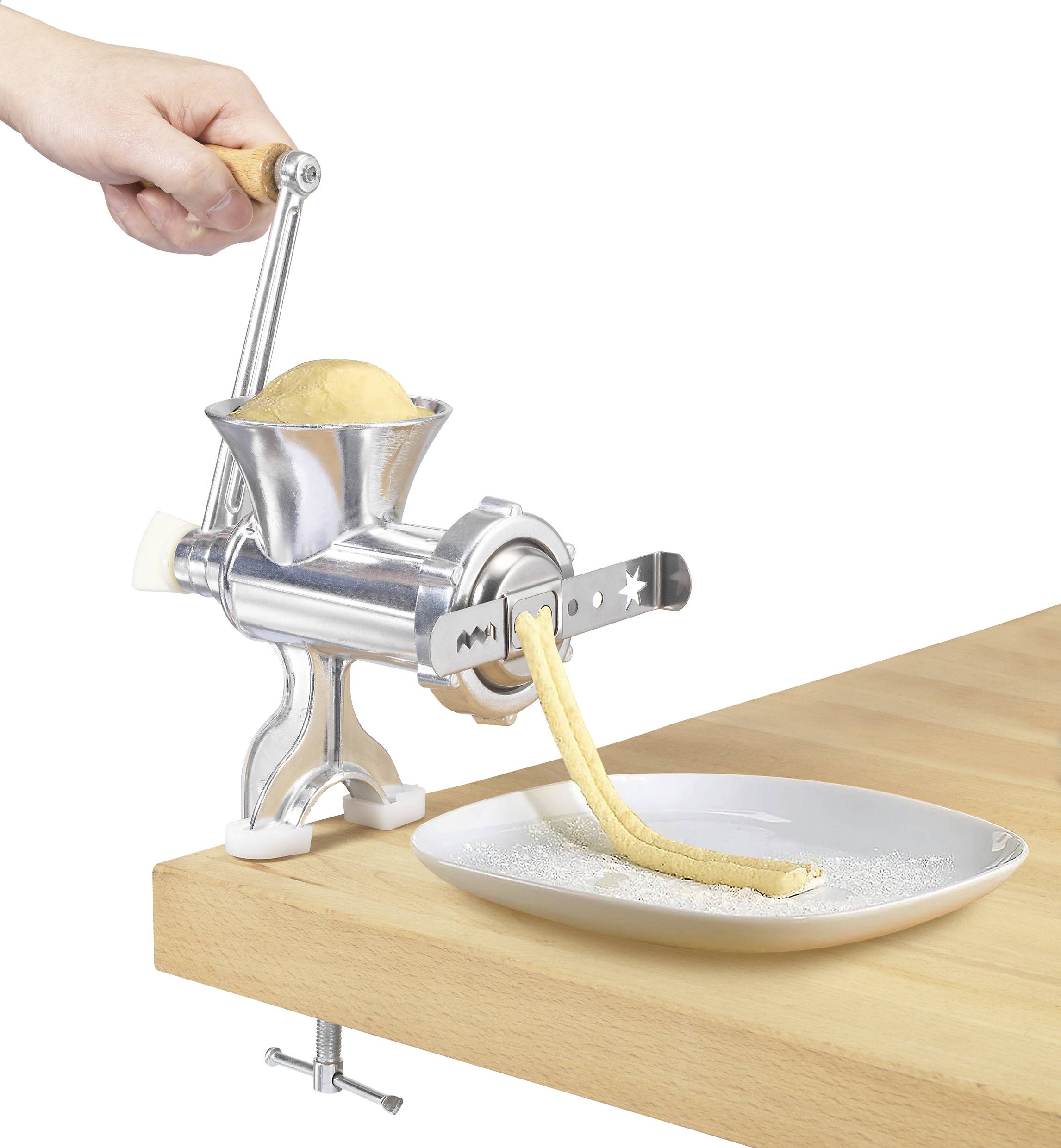 Een hand draait een oude metalen pastamachine die deeg uitrolt. Het deeg valt op een bord op een houten tafel.