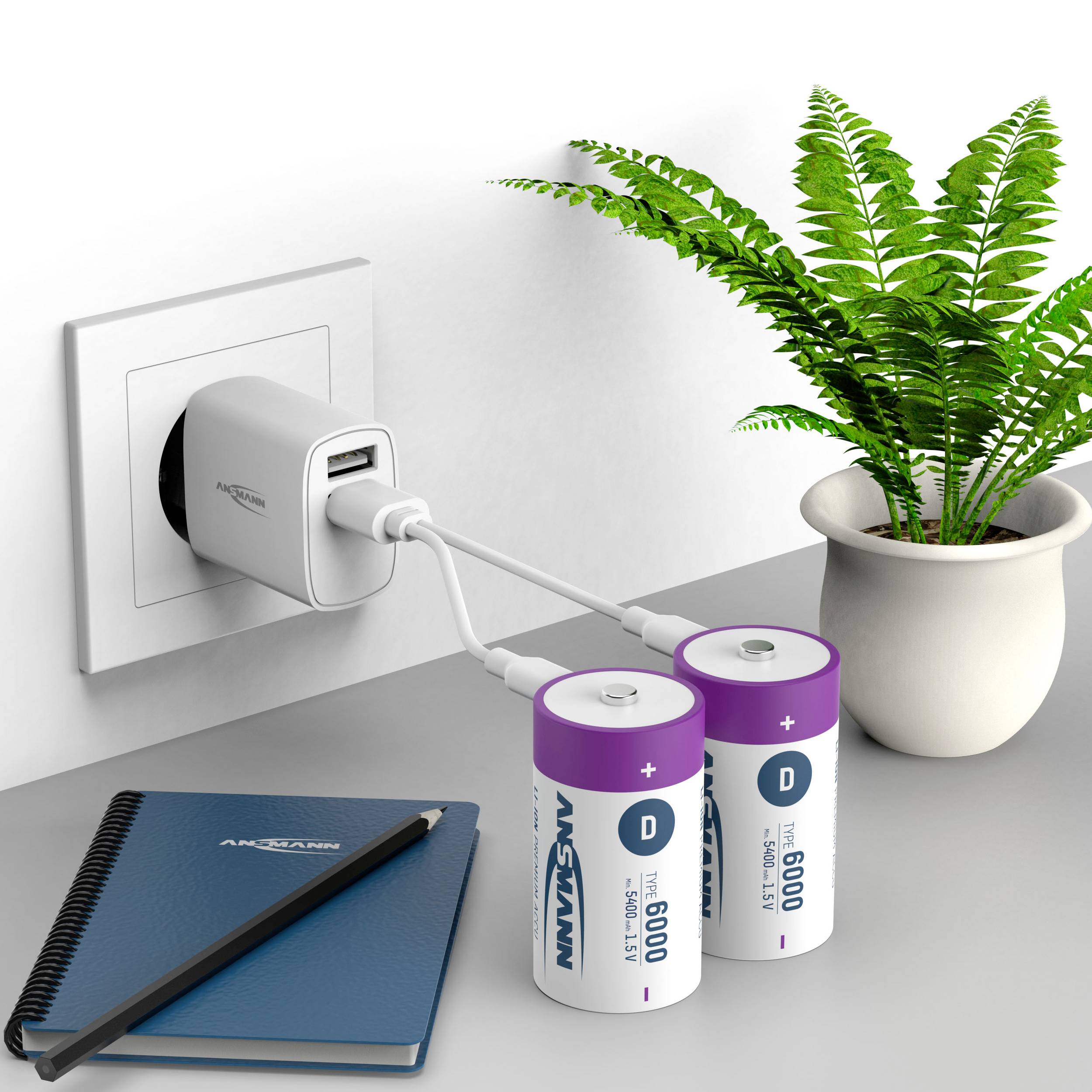 Een stopcontact met een oplader laadt twee grote, batterijvormige powerbanks op. Ernaast liggen een notitieboek en een pen.