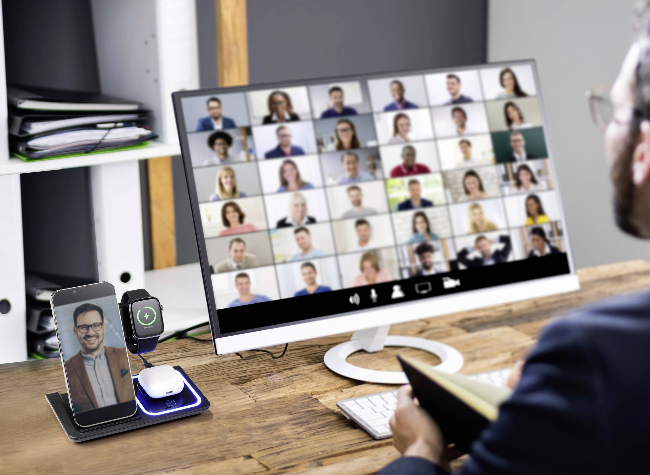 Een persoon neemt deel aan een videoconferentie met veel deelnemers op een computerscherm. Een mobiele telefoon toont dezelfde oproep.