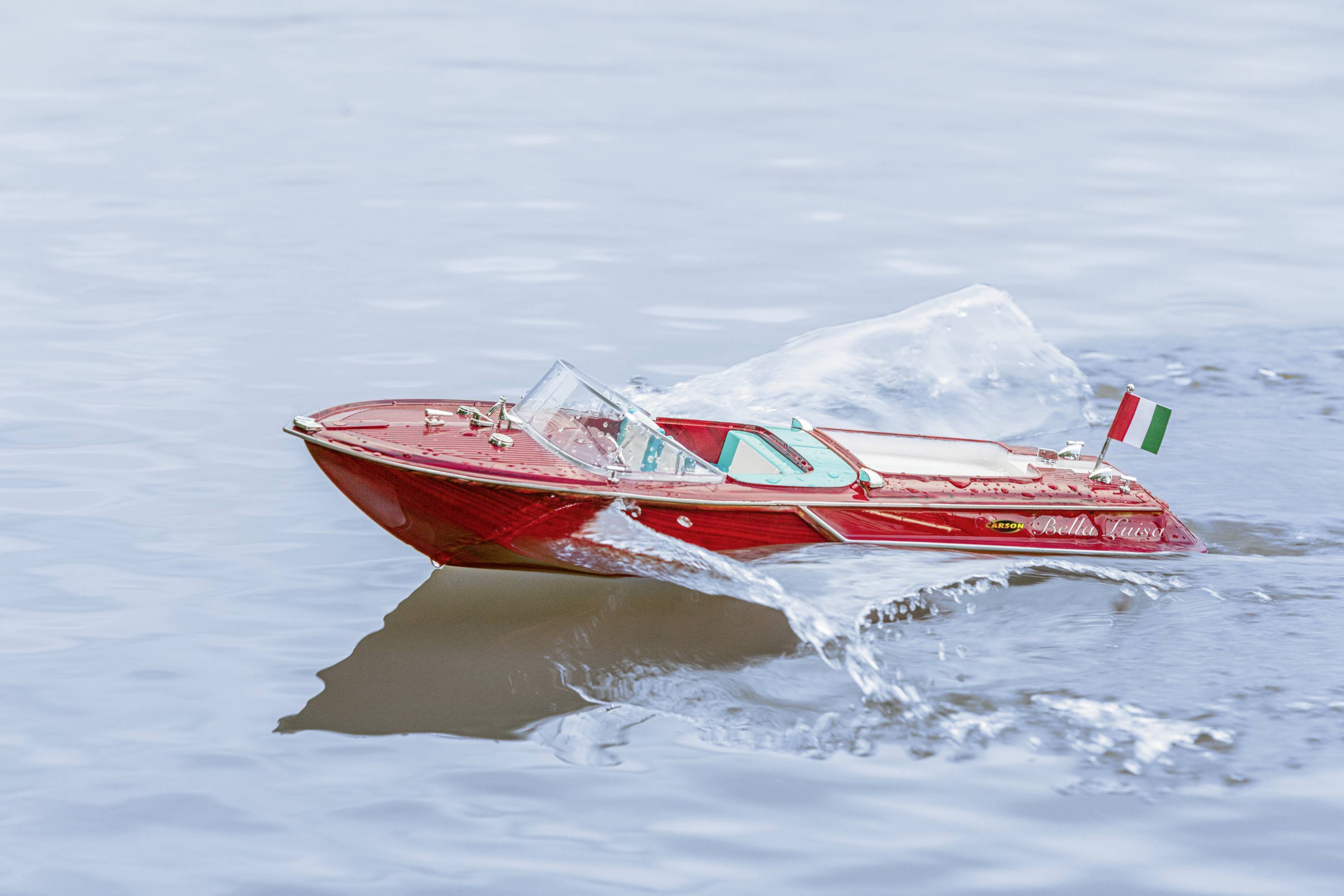 Een rood modelsnelheidsboot vaart op het water, met een kleine Italiaanse vlag aan de achterkant.