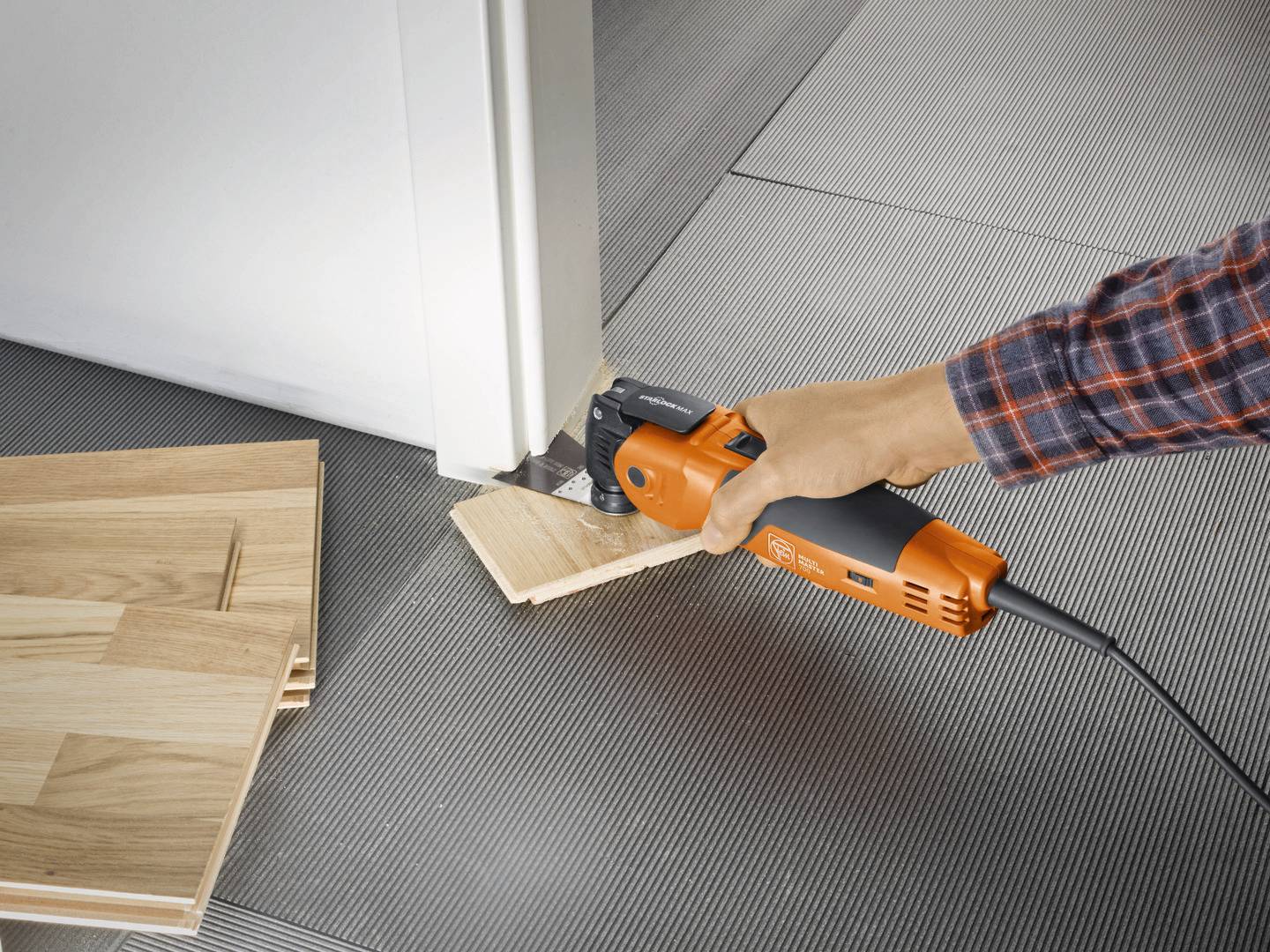 Een persoon zaagt houten latten aan een deurkozijn met een oscillerend elektrisch gereedschap om vloerplaten eronder te kunnen leggen.