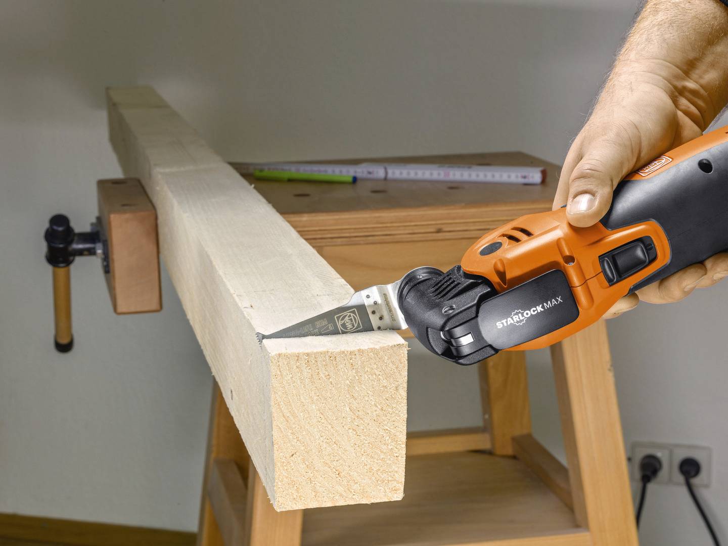 Een hand houdt een oscillerend gereedschap vast en snijdt nauwkeurig een rechthoekig houten bord dat is vastgeklemd in een werkbank.