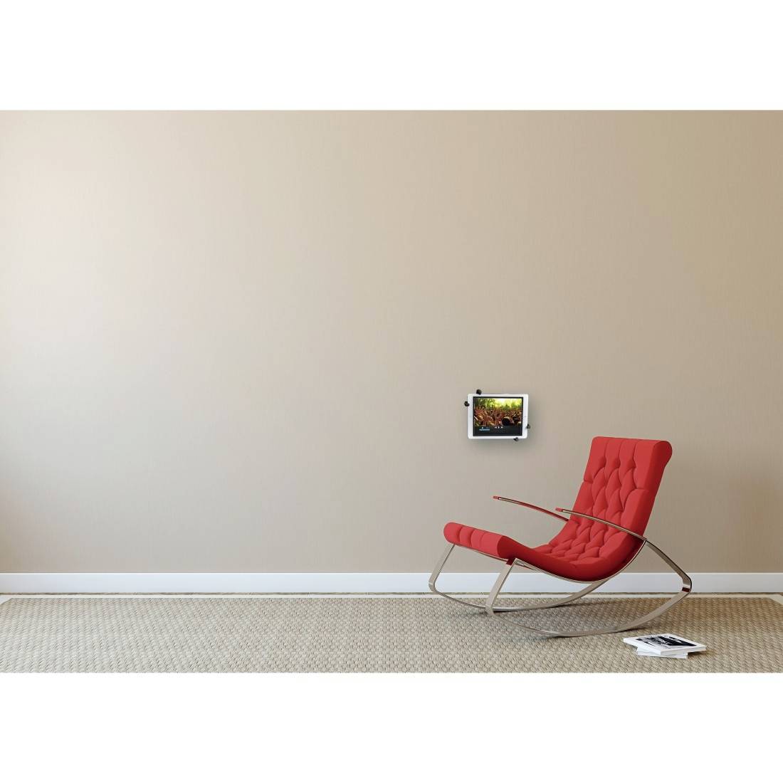 Een rode schommelstoel staat in een minimalistische ruimte met beige muren. Aan de muur hangt een klein, helder verlicht kunstwerk.