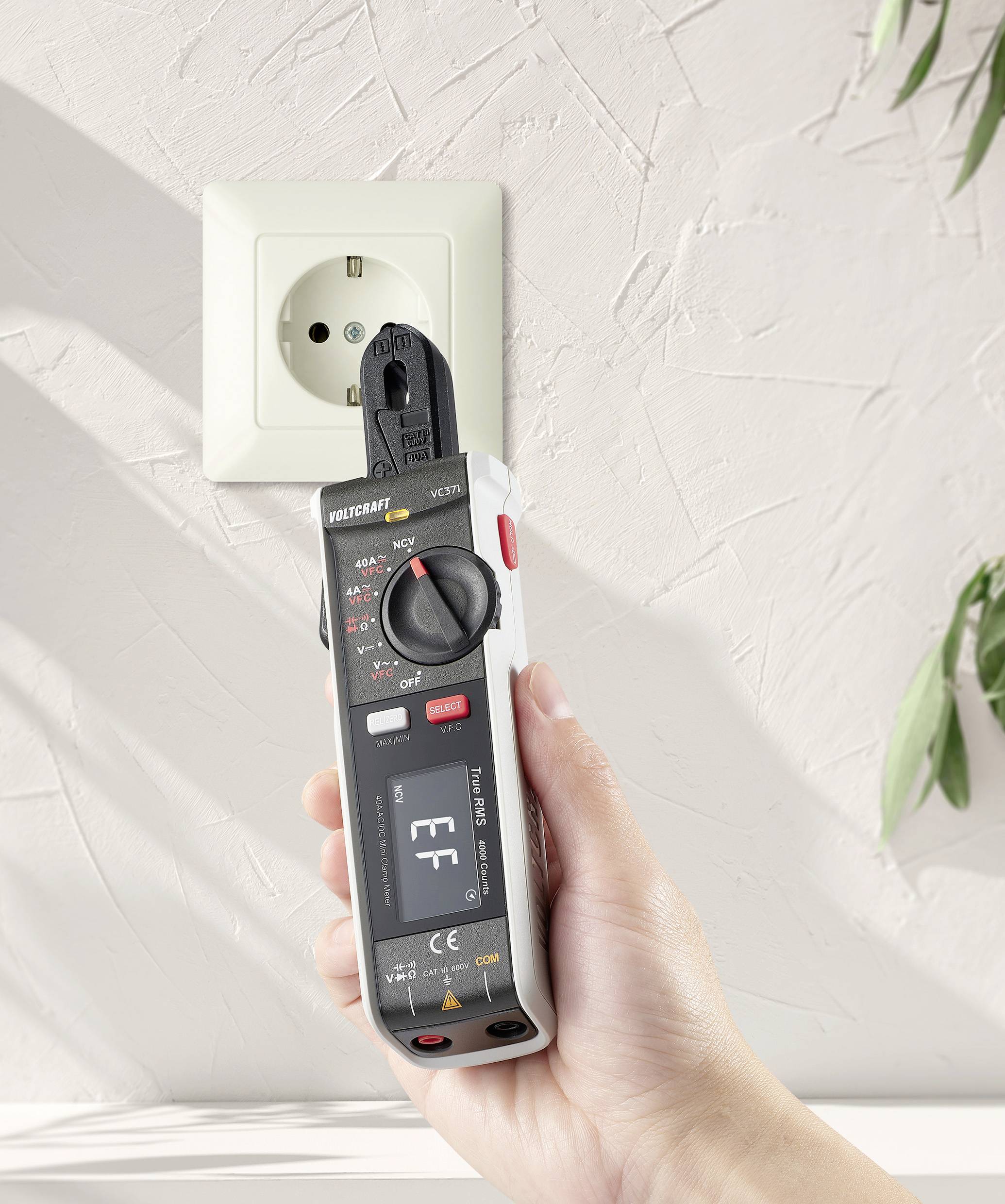 Een hand houdt een multimeter vast bij de stekker van een stopcontact om de spanning te controleren.