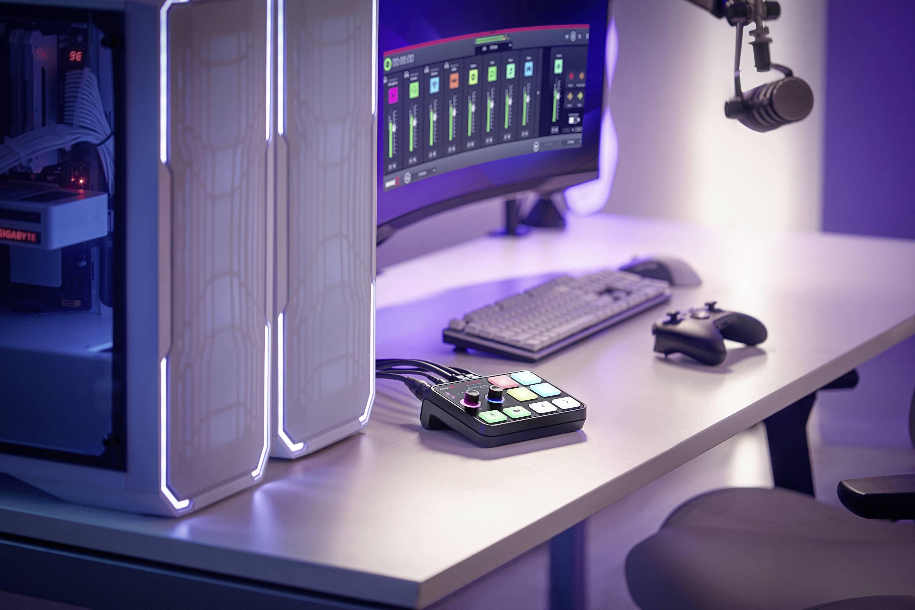 Een moderne computertafel met een groot beeldscherm, toetsenbord, microfoon, controller en audiomengpaneel op een verlicht bureau.