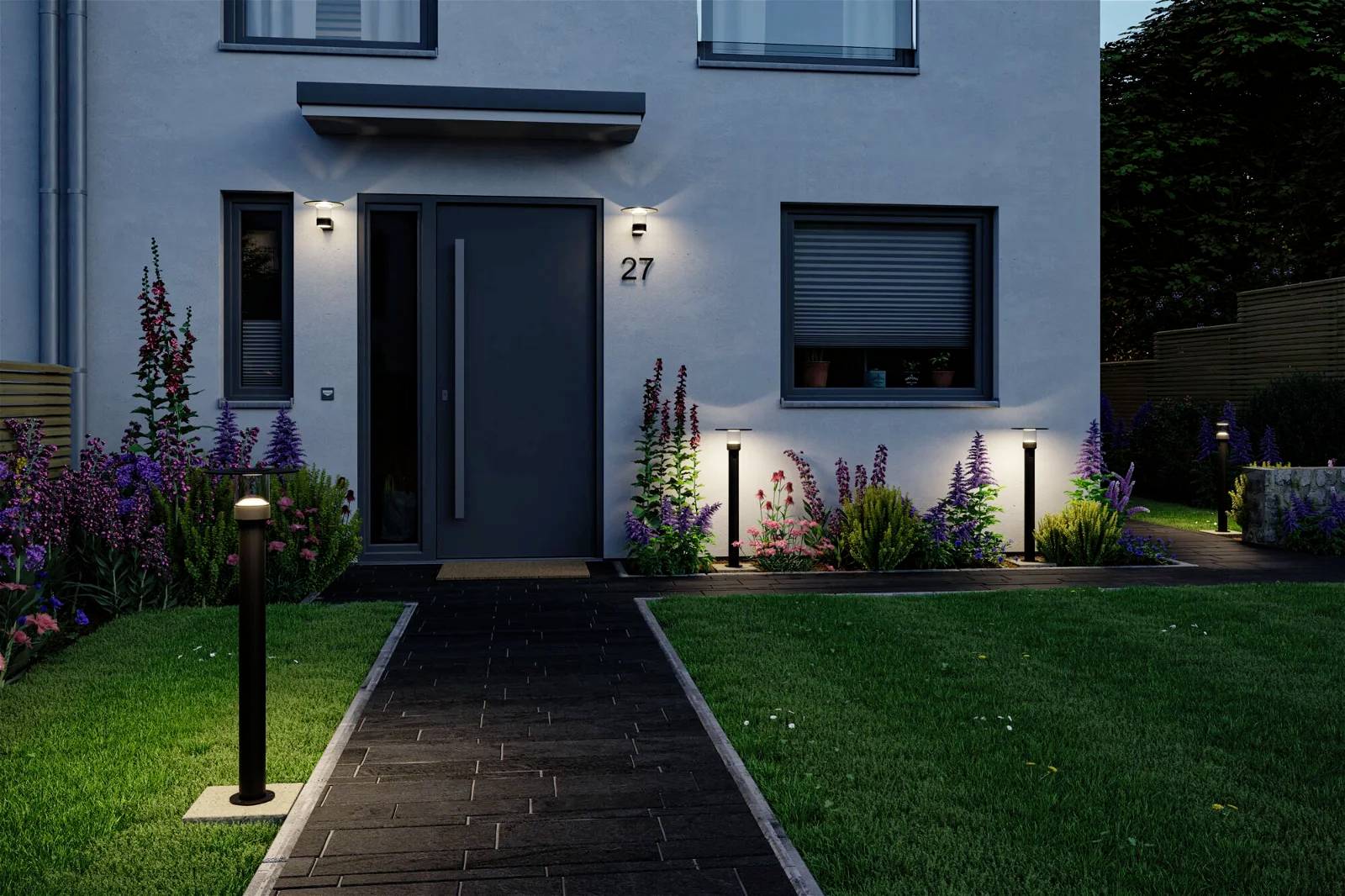 Entree van een modern huis 's avonds, verlicht met tuinverlichting. Omgeven door een verzorgd gazon en kleurrijke bloemen.