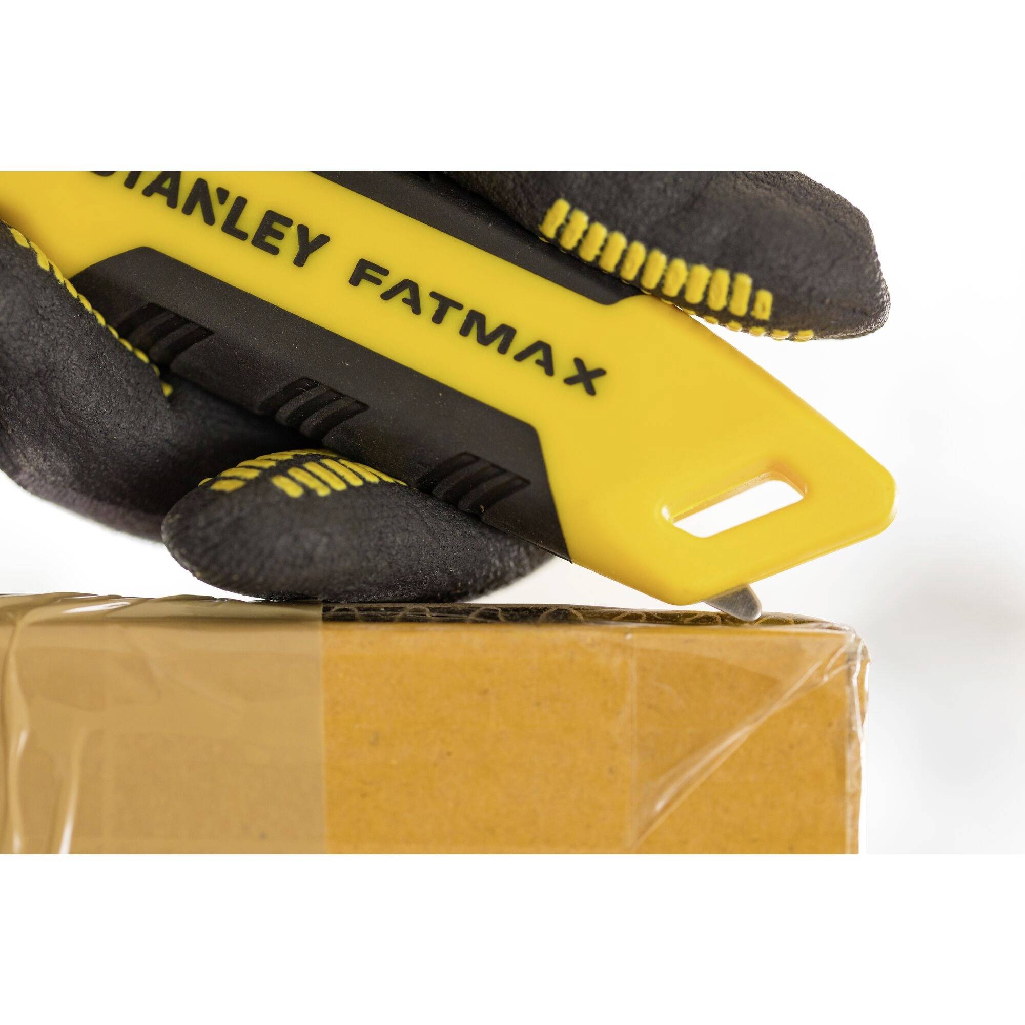 Hand met een zwarte handschoen houdt een geel Stanley Fatmax mes en snijdt een bruine doos open.