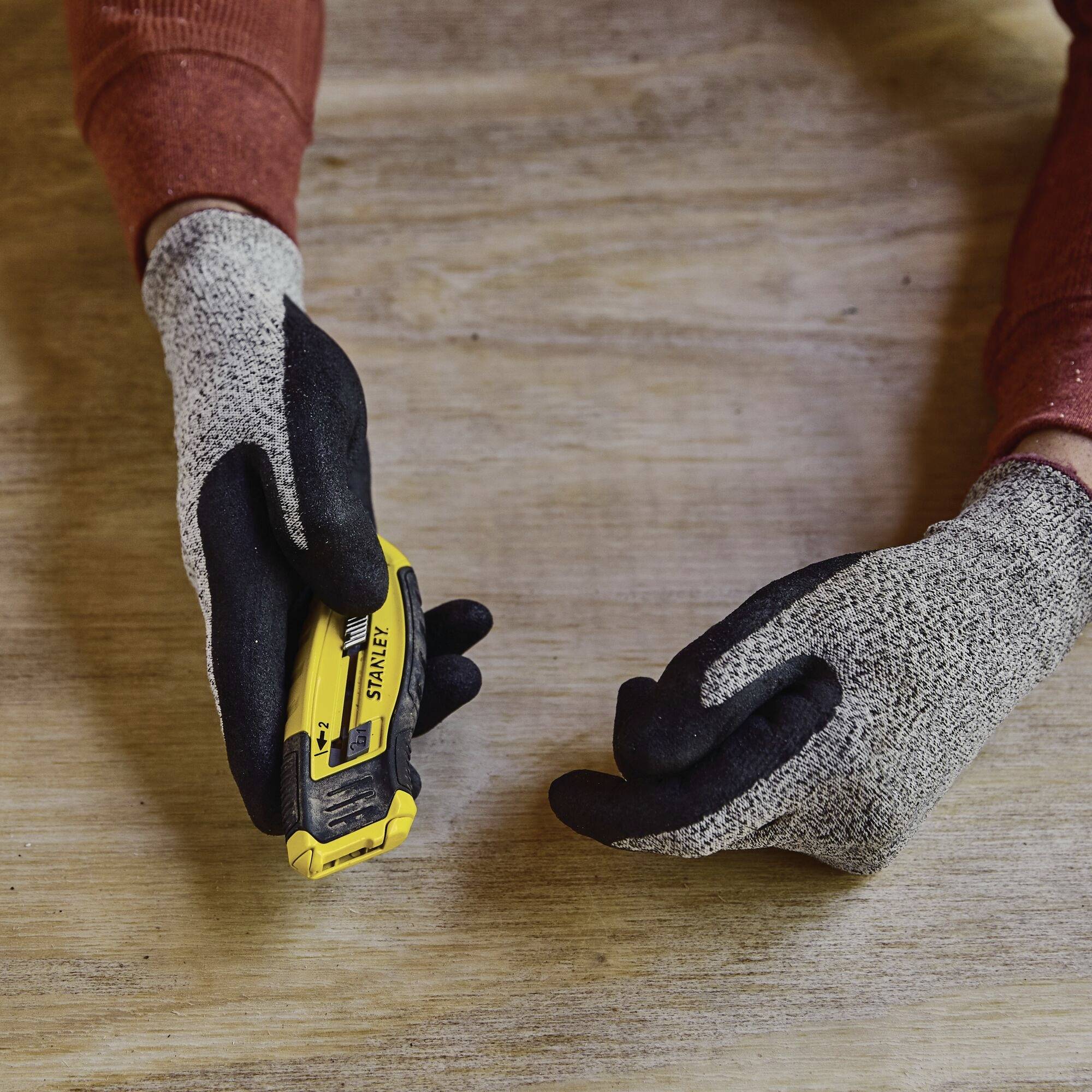 Twee handen met werkhandschoenen houden een geel meetlint vast op een houten tafel.