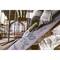 Een persoon met werkhandschoenen snijdt met een geel breekmes een grote, gebogen metalen plaat op een bouwplaats.
