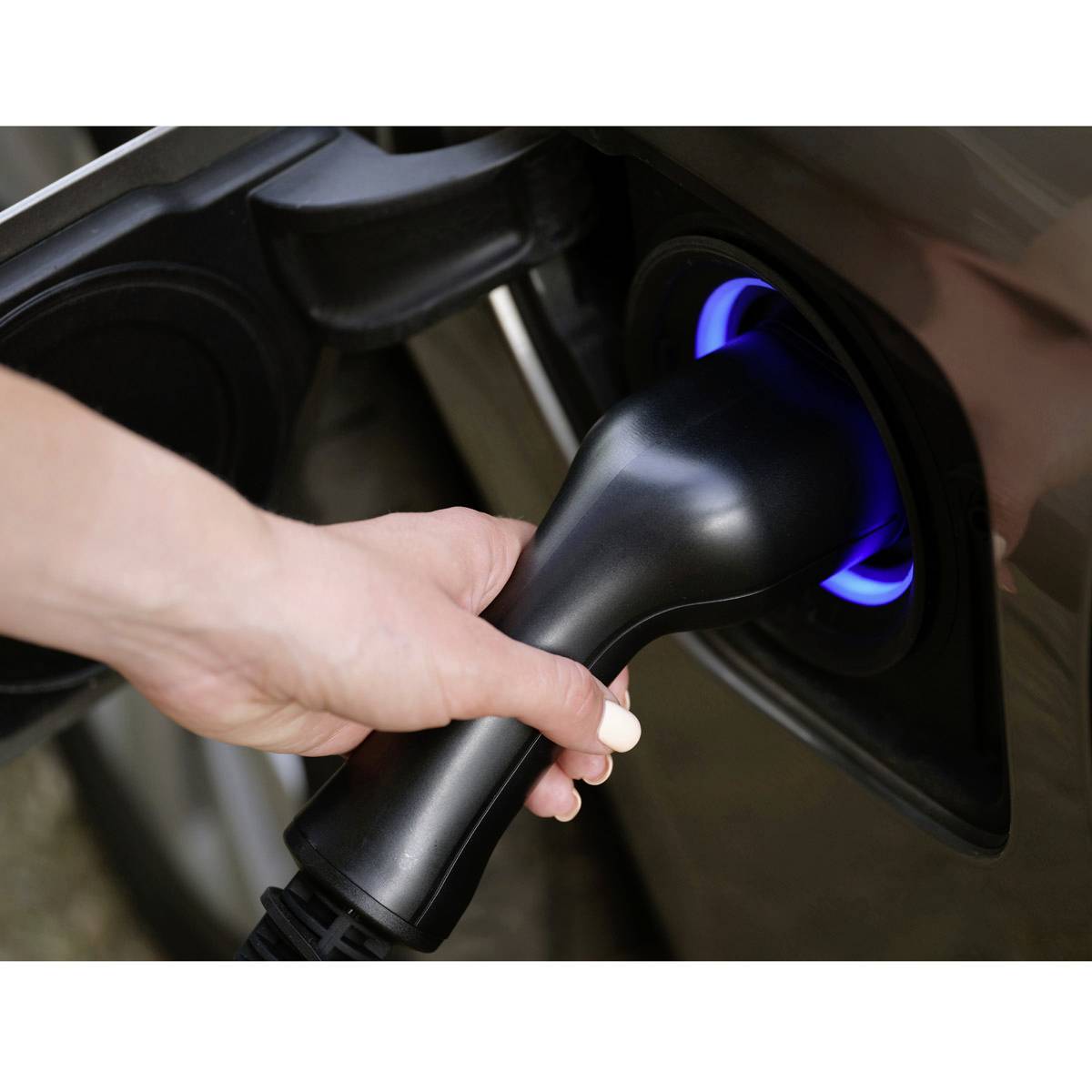 Een hand steekt een oplaadkabel in een elektrisch voertuig. Een blauwe lichtcirkel geeft de laadstatus aan.