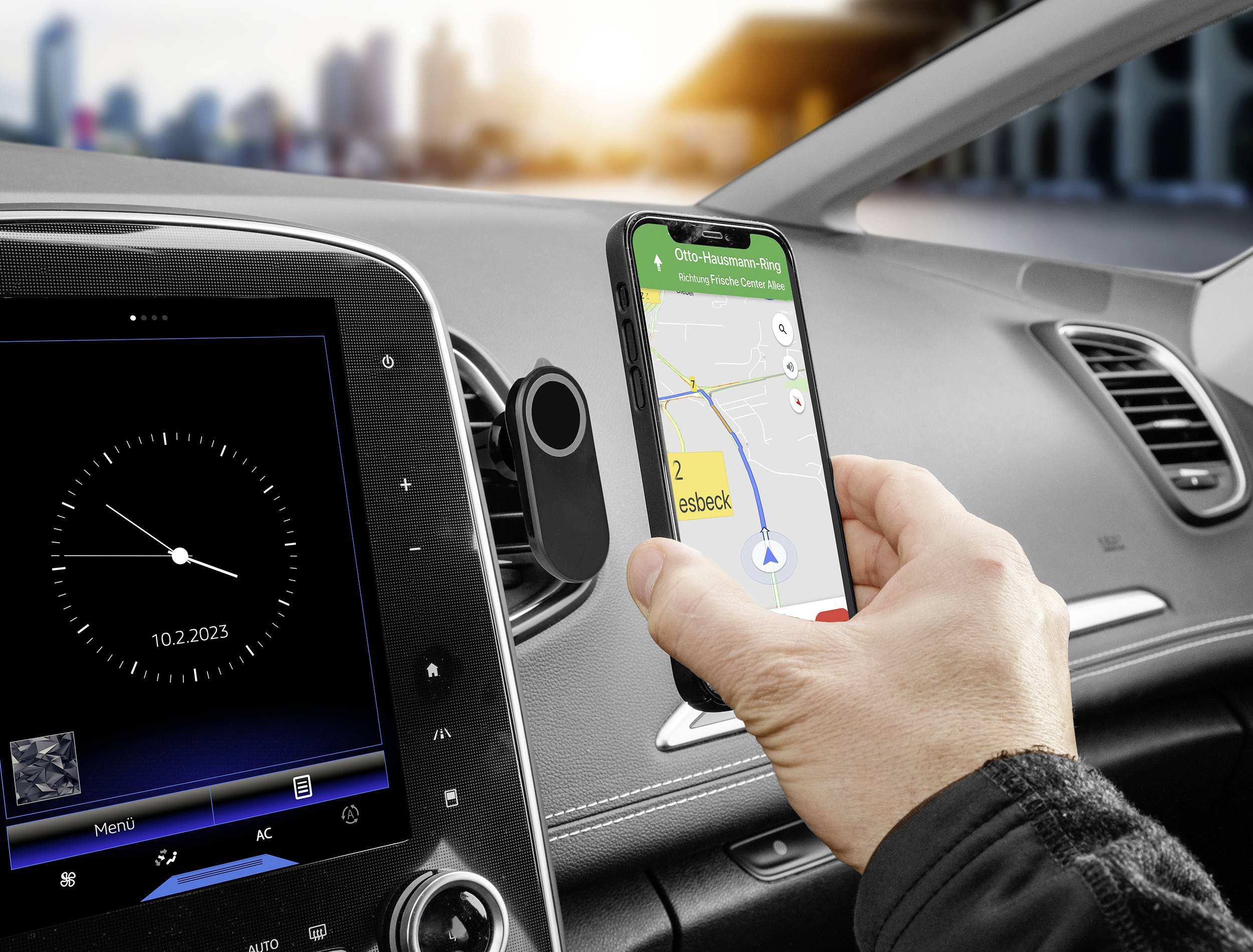 Een persoon houdt een smartphone met een navigatie-app vast in de auto, die een route naar een bestemming weergeeft. Op de achtergrond zijn gebouwen zichtbaar.