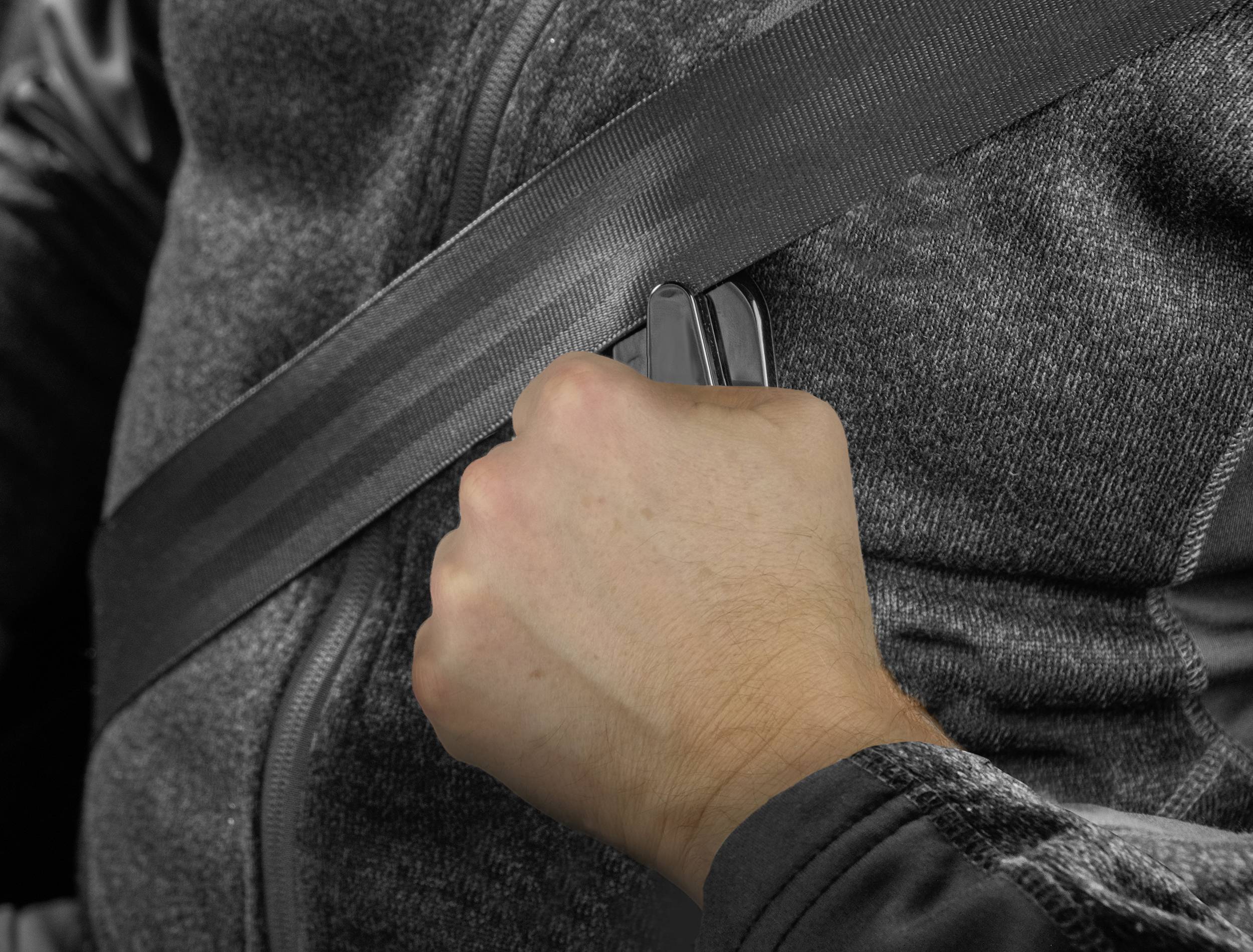 Een persoon draagt een autoveiligheidsgordel en grijpt met de rechterhand naar de veiligheidsgordelsluiting.