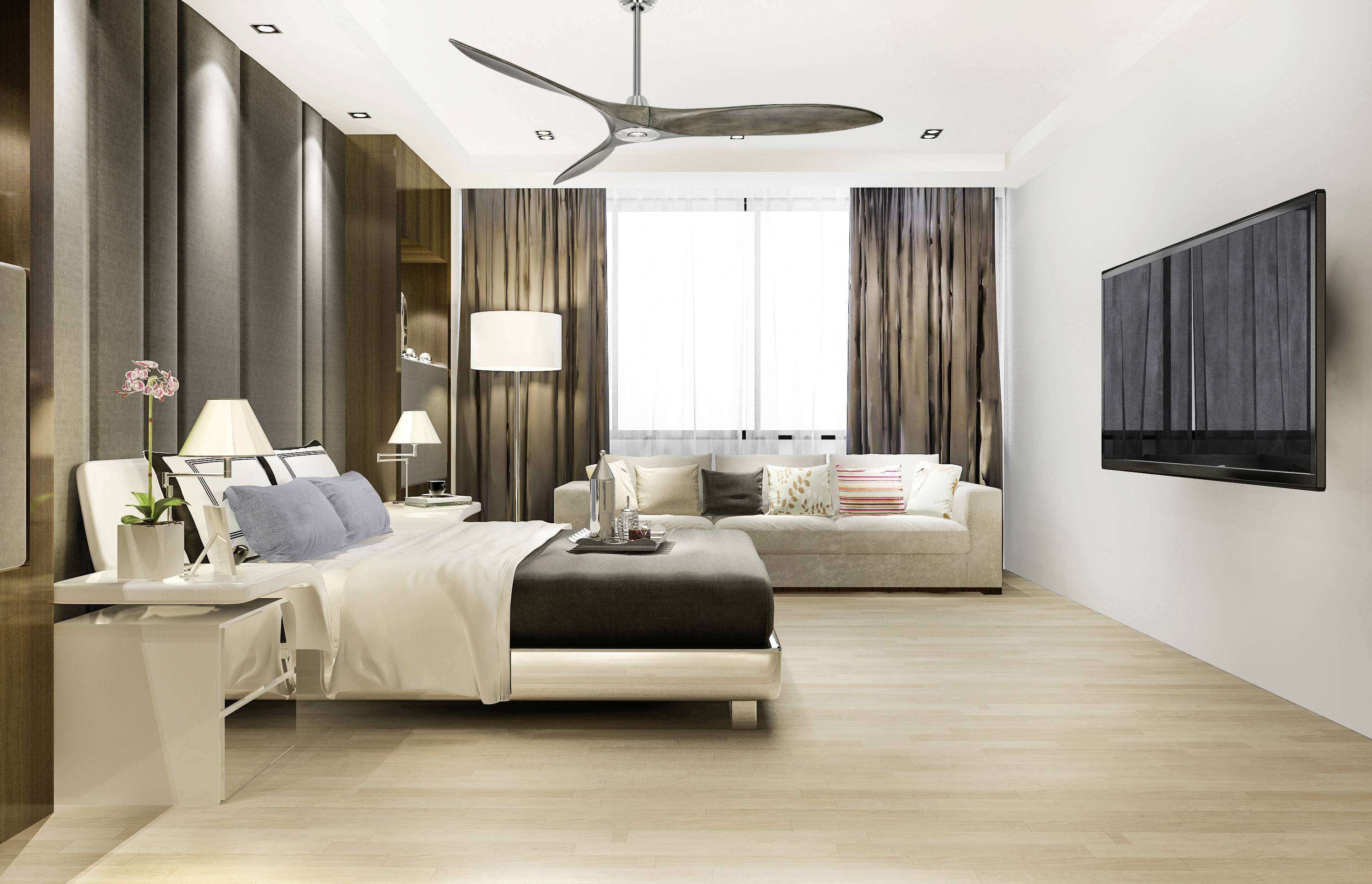 Moderne slaapkamerperspectief met tweepersoonsbed, bank, grote tv aan de muur en plafondventilator; goed verlicht en stijlvol.