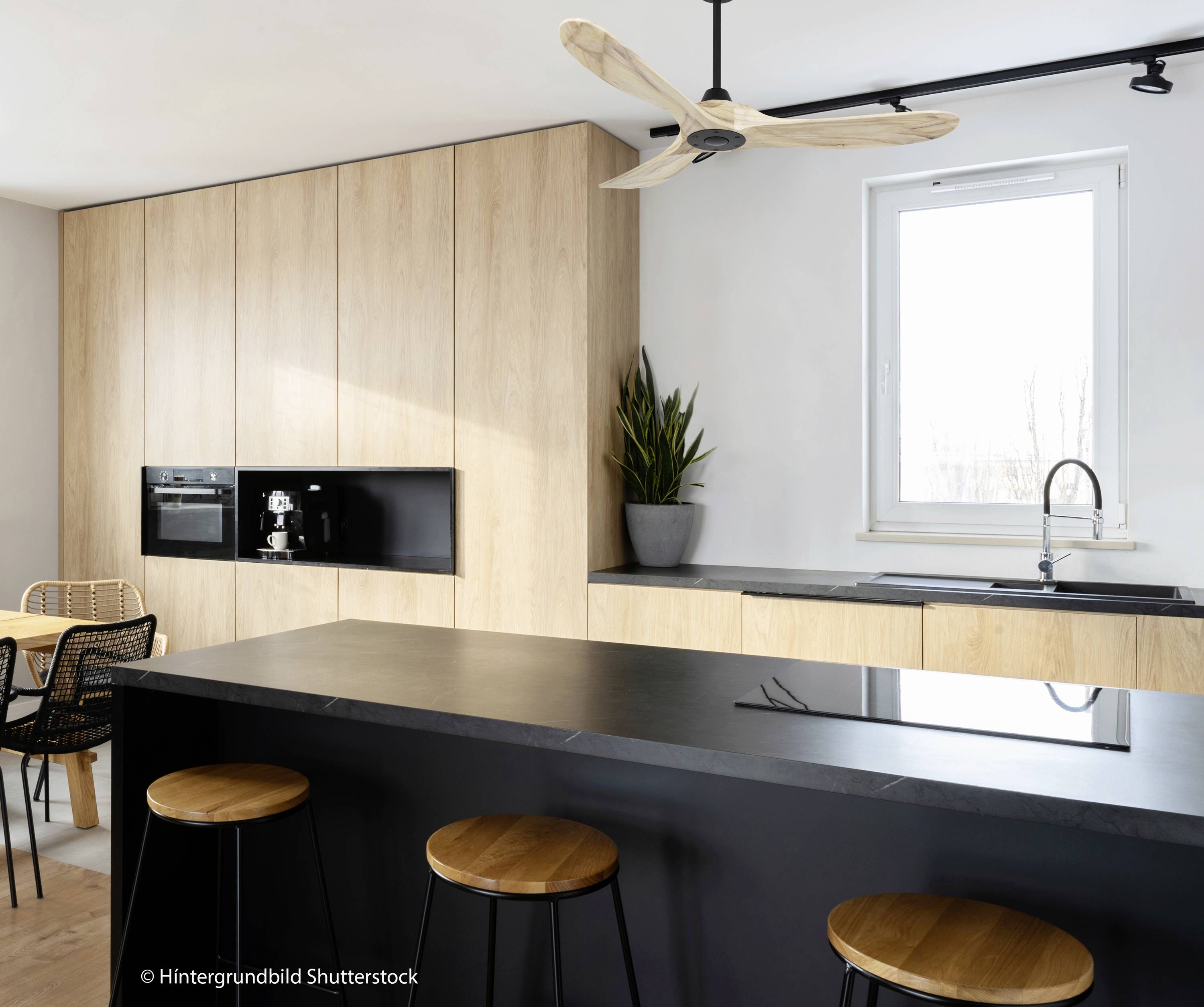 Moderne keuken met een zwart werkblad, houten kasten, een kleine ronde tafel en stoelen. Een groot raam zorgt voor veel licht.