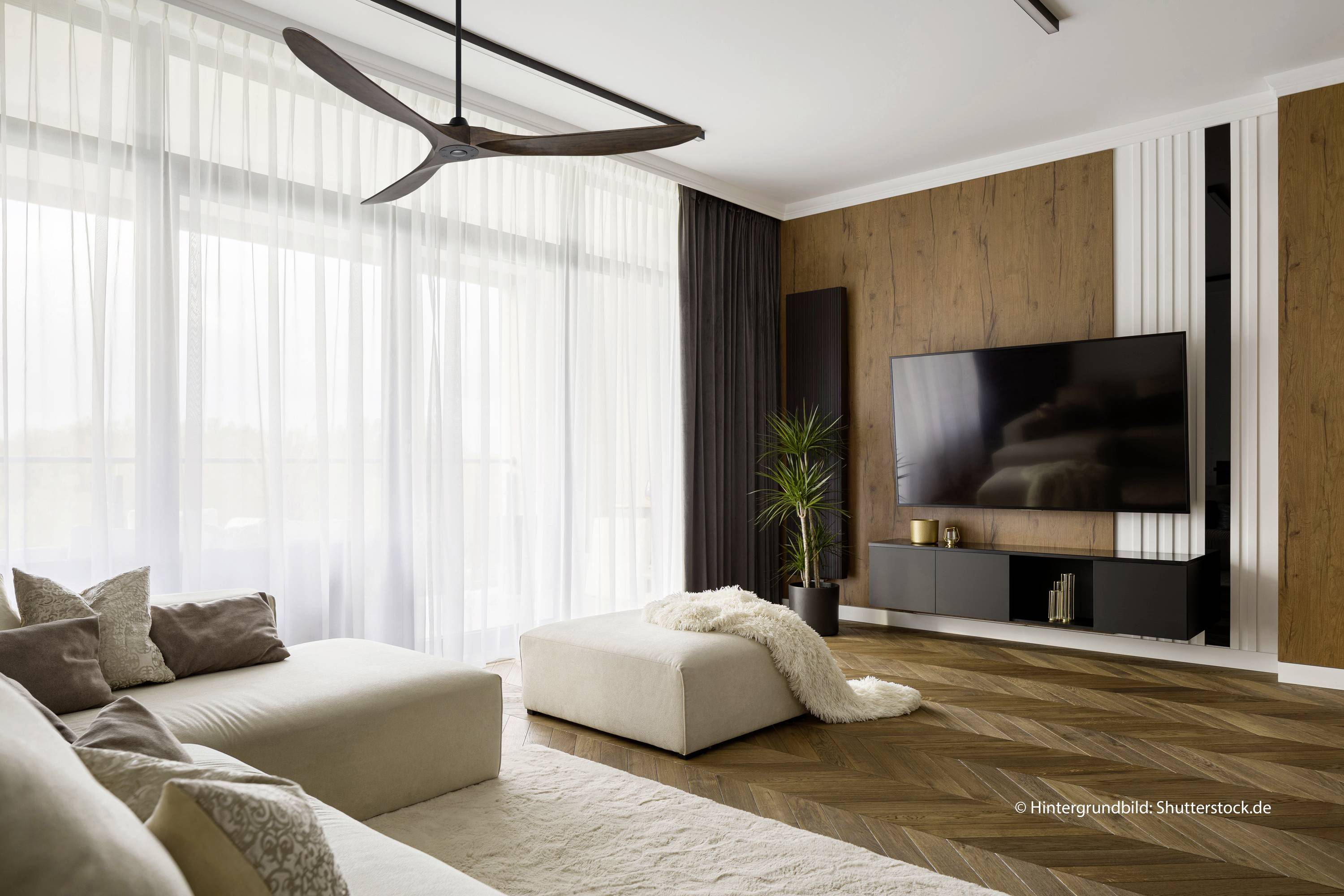 Modern woonkamer met een groot bank, een gezellig tapijt, een televisie aan een houten wand en grote ramen die veel licht binnenlaten.