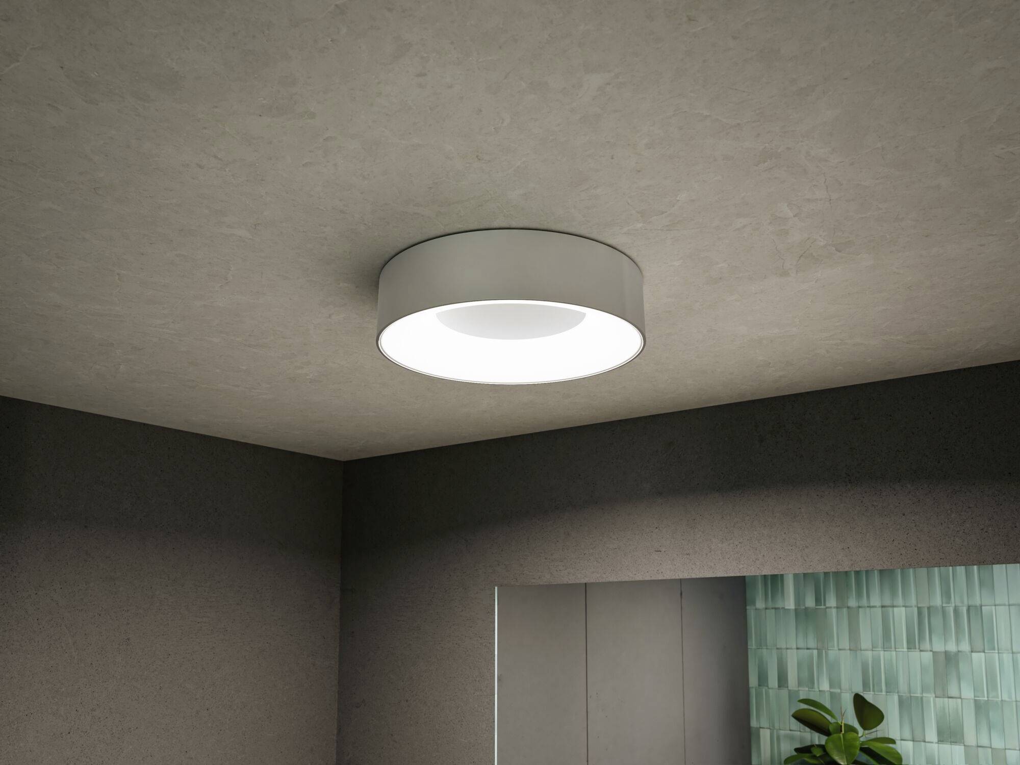 Een ronde plafondlamp verlicht het grijze plafond in een moderne ruimte. Op de achtergrond is een muur met groene tegels zichtbaar.