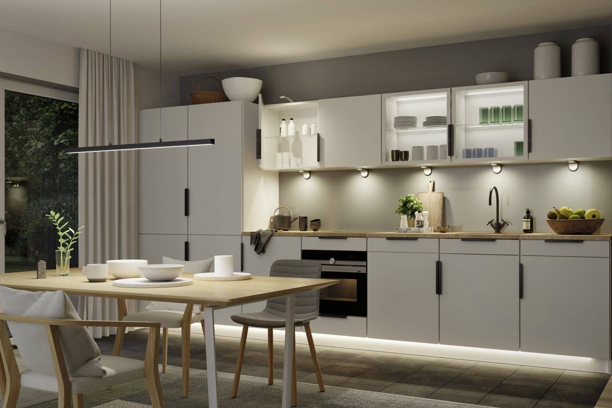 Moderne keuken met eettafel, stoelen en minimalistische inrichting. Lichte kasten met geïntegreerde verlichting, fruitschaal op het aanrecht.