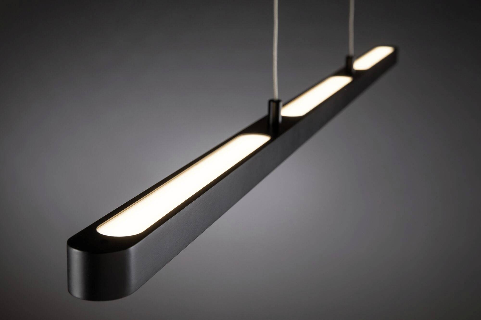 Hangende LED-lamp in langwerpige, zwarte behuizing, verlicht in een donkere ruimte. Focus op modern en minimalistisch design.