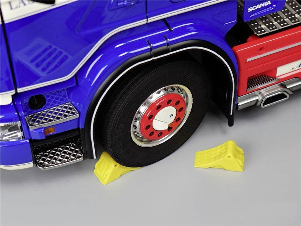 Een blauwe vrachtwagen met een gele wielkeg achter de band om het rollen te voorkomen. Band met een rode wielkap.