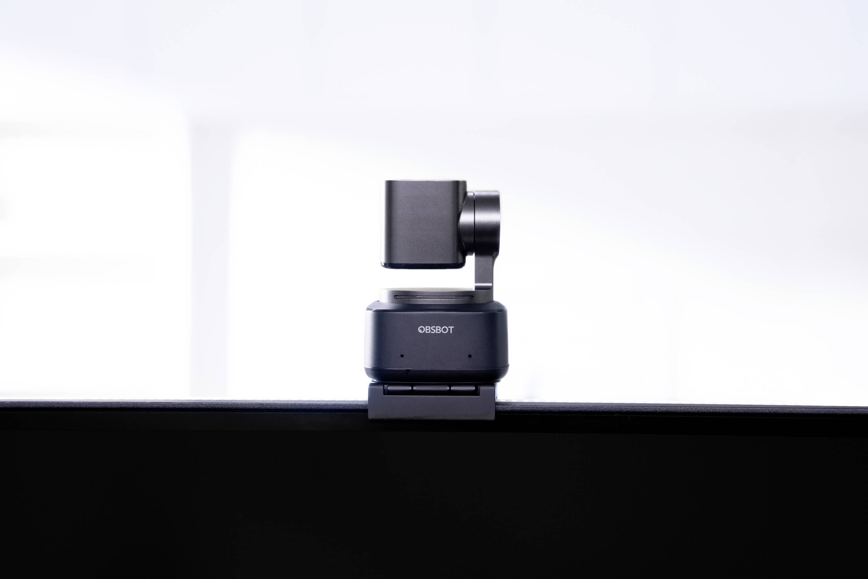 Een kleine, draaibare camera zit op een beeldscherm. De camera is gemonteerd op een stabiele voet en fotografeert in een lichte ruimte.