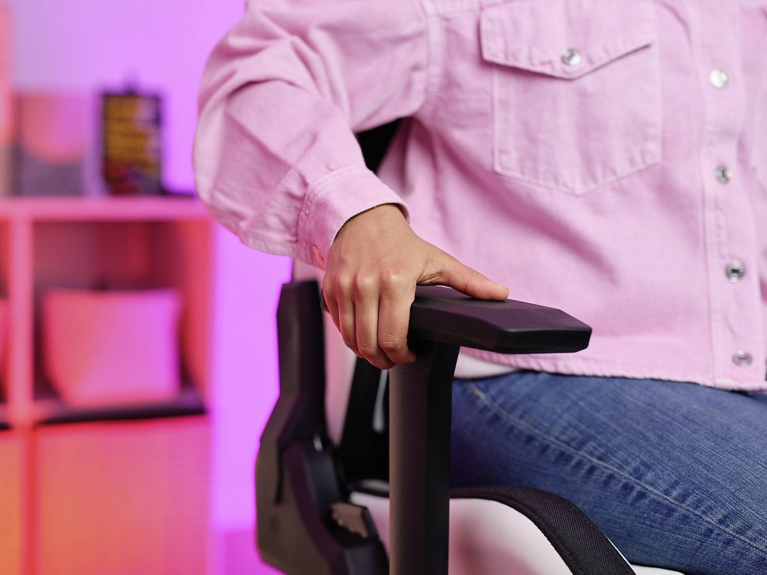 Een persoon zit op een bureaustoel in een ruimte met roze achtergrondverlichting. Ze houdt haar arm op de armsteun van de stoel.