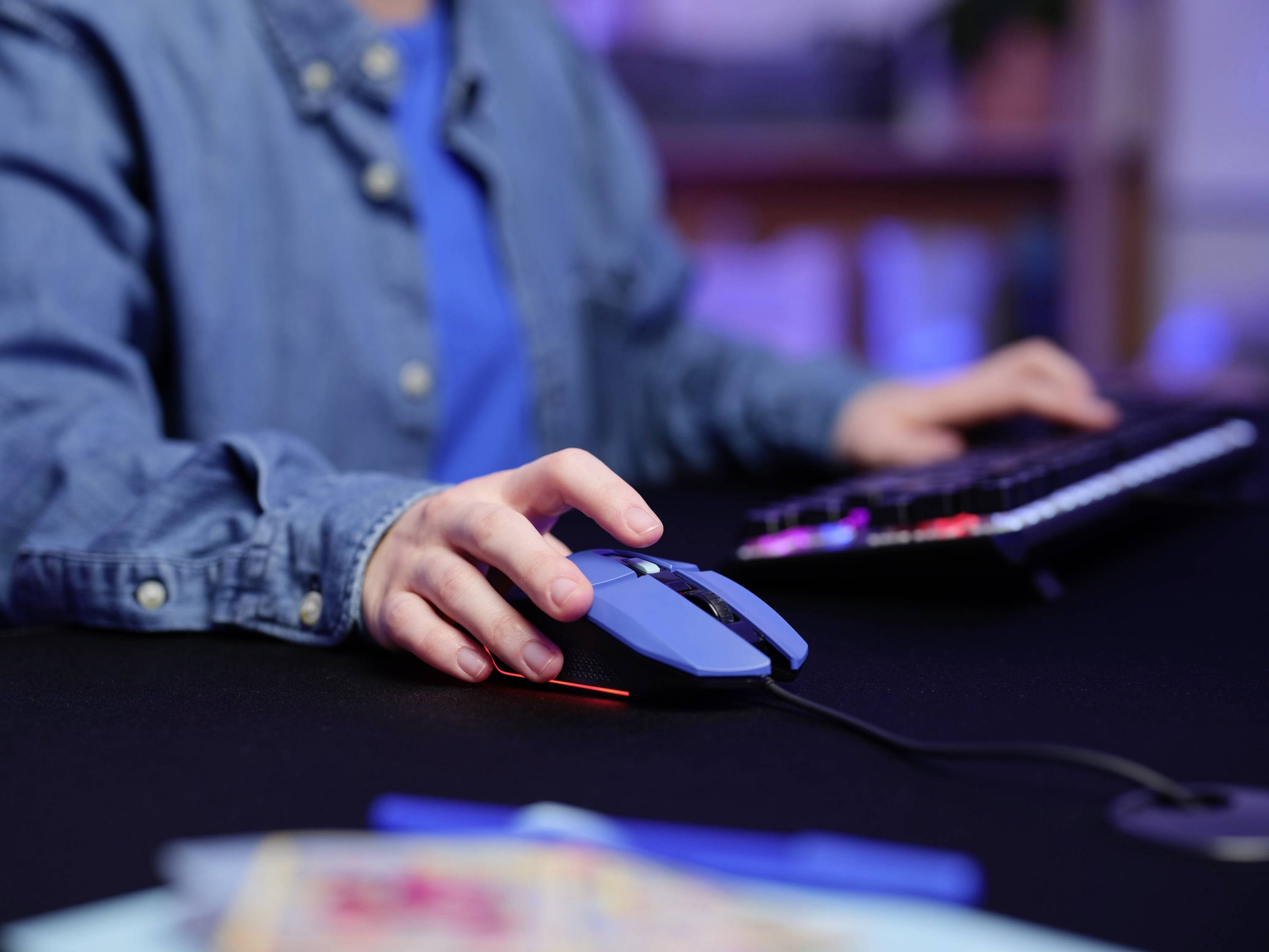 Persoon in blauwe kleding gebruikt een computermuis en toetsenbord op een bureau. Kantooromgeving op de achtergrond.