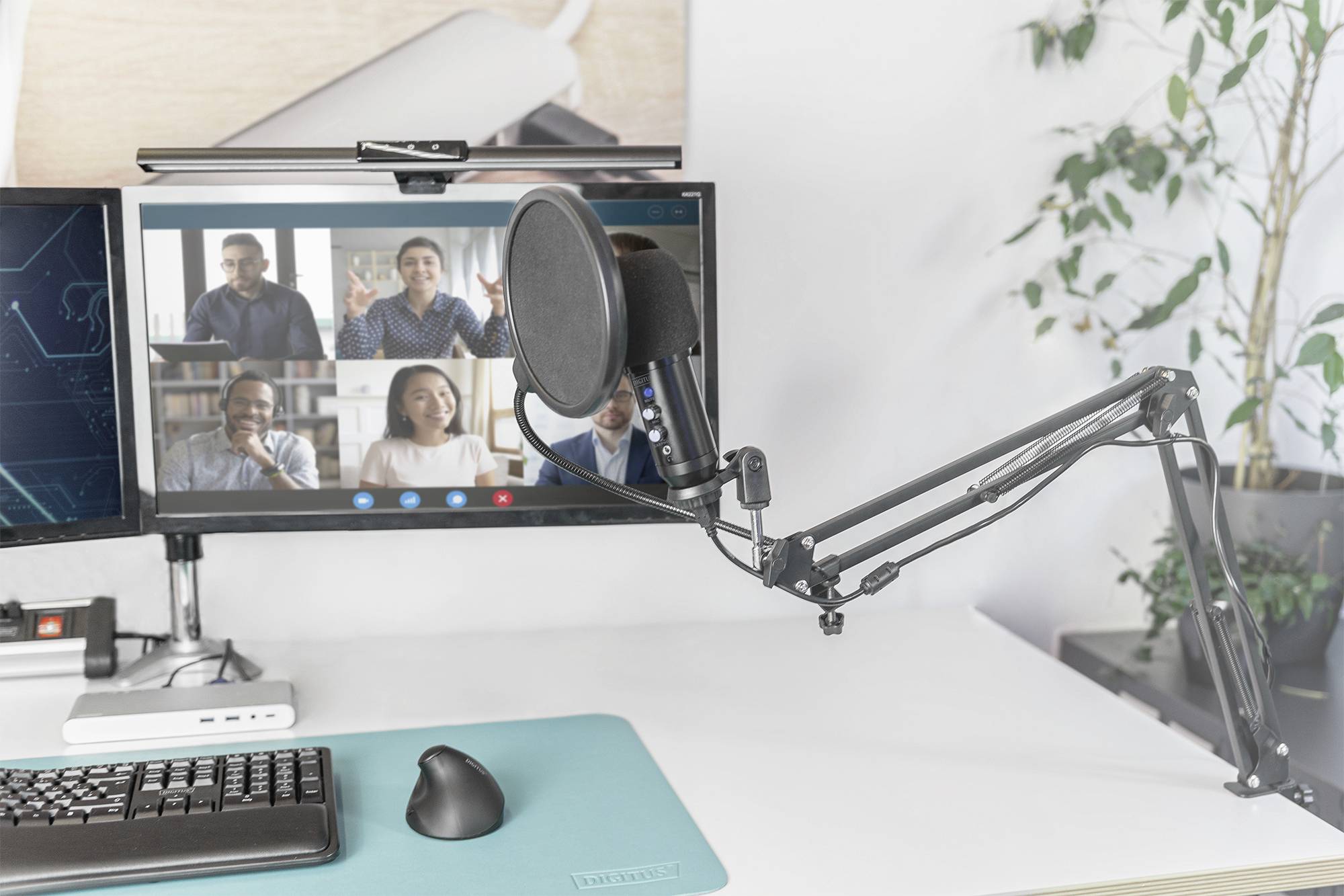 Thuiskantoor met monitor toont videoconferentie met vijf personen, microfoonarm bevestigd aan de tafel, moderne en professionele omgeving.