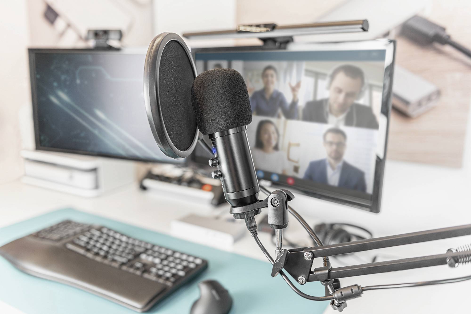 Een microfoon op een bureau voor een computerscherm dat een videoconferentie met vier personen weergeeft.