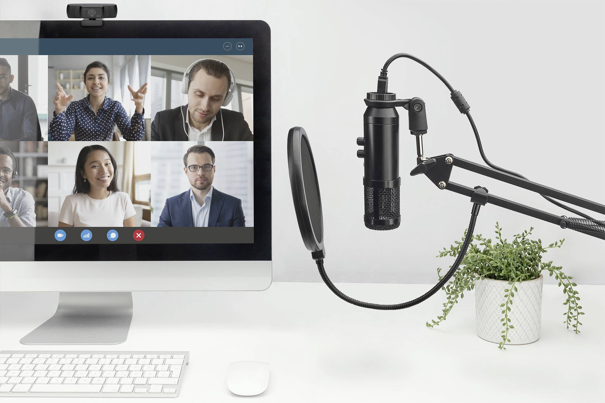 Een computerscherm toont een videogesprek met meerdere personen. Naast het scherm staat een microfoon, klaar om te worden gebruikt.