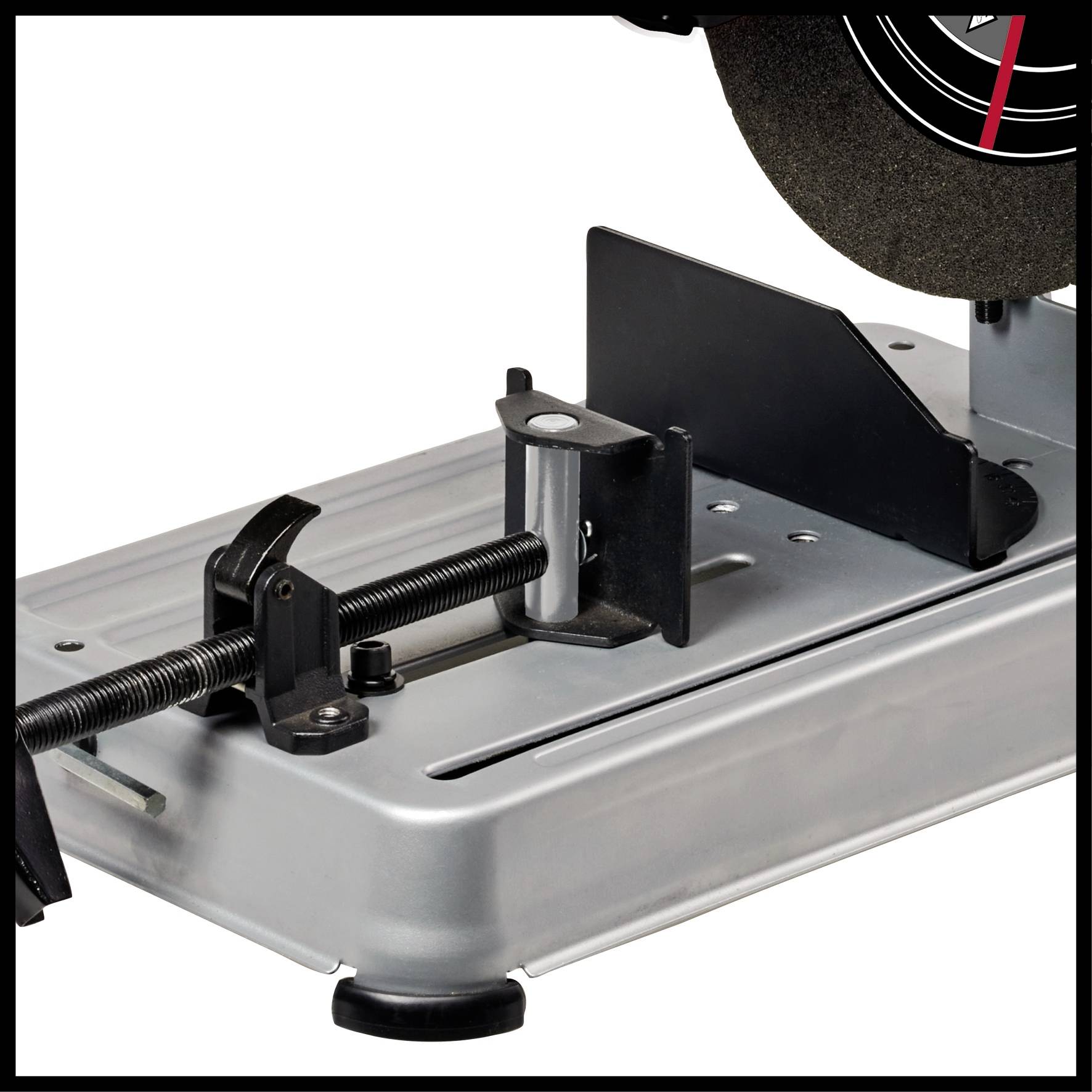 Een zilveren metalen klem op een gereedschapstafel, met een zwaar zwart snijwiel rechtsboven. Werkplaatsomgeving.