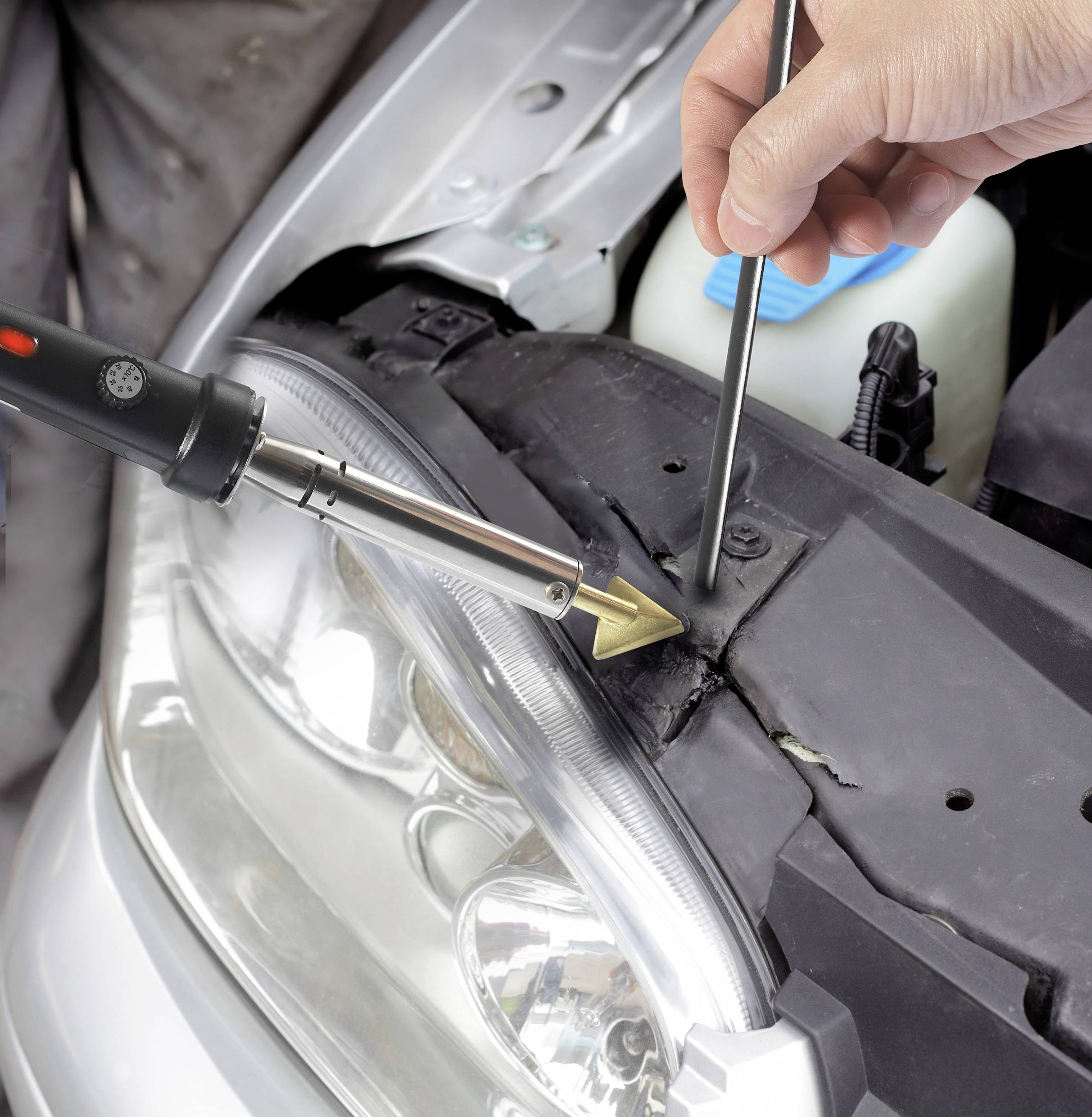 'Iemand repareert het kunststof aan een auto-onderdeel met een soldeerbout en een gereedschap dat druk uitoefent om het materiaal te vormen.'