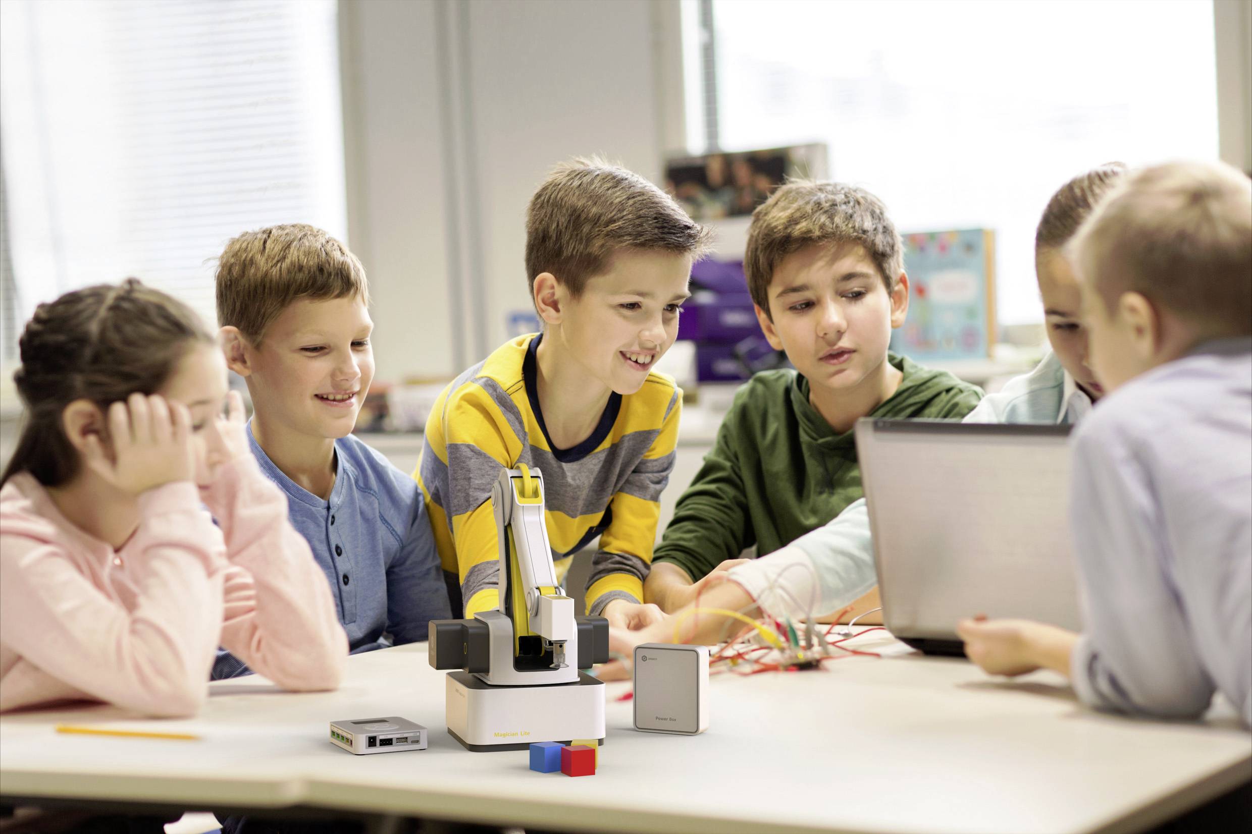 Kinderen werken samen aan een tafel met een laptop en elektronische componenten in een klaslokaal.