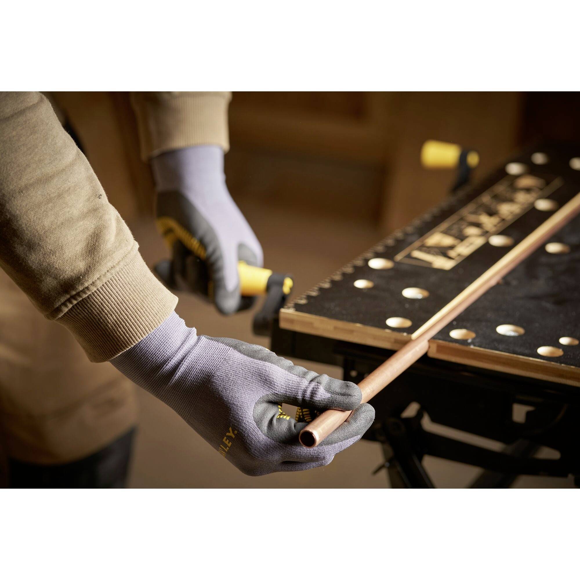 Een persoon houdt en snijdt een koperen buis met een pijpsnijder. Hij draagt handschoenen en werkt aan een werkbank.