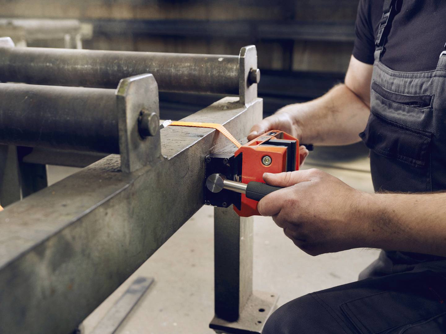 Een persoon in werkkleding stelt met een meetinstrument de afstand tussen twee metalen rollen in een werkplaats af.