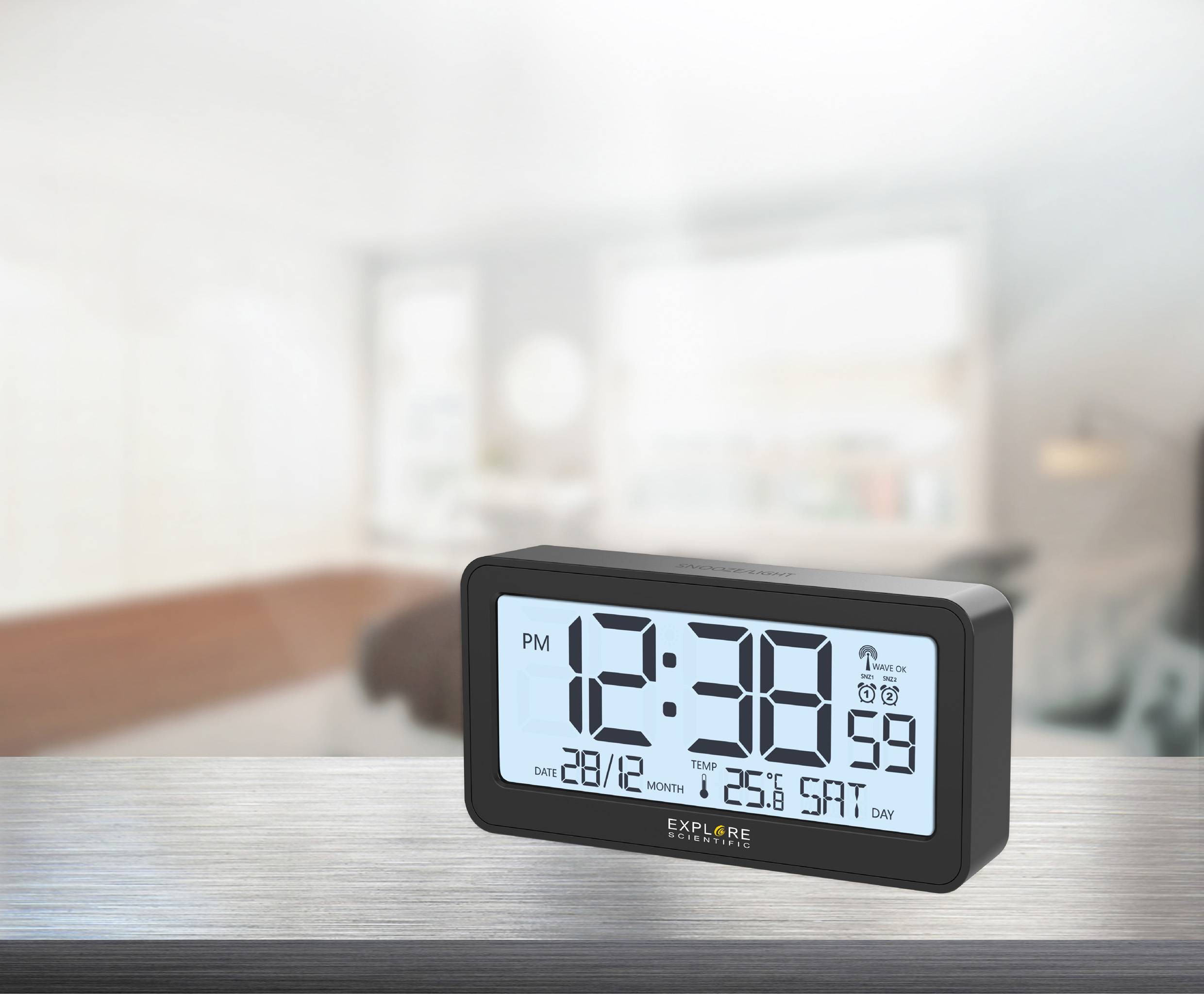 Een digitale klok toont de tijd 12:38 's middags, met datum 28/12, maand 12, en zaterdag als weekdag. Hij staat op een tafel in een kamer.