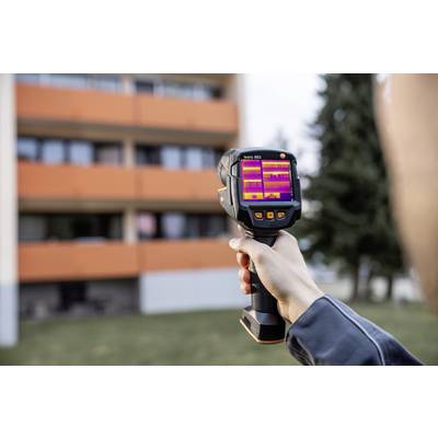 Een persoon houdt een warmtebeeldcamera en meet de temperatuur van een gebouw op afstand.
