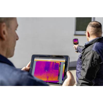 Twee mannen voeren een warmtebeeldonderzoek uit aan een muur, waarbij een van hen een tablet vasthoudt met een kleurenscherm en de ander een camera.