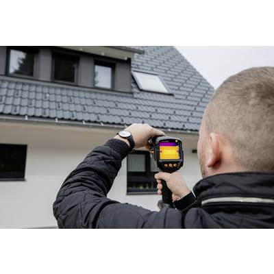 Een persoon houdt een warmtebeeldcamera voor een huis en controleert de dakisolatie.