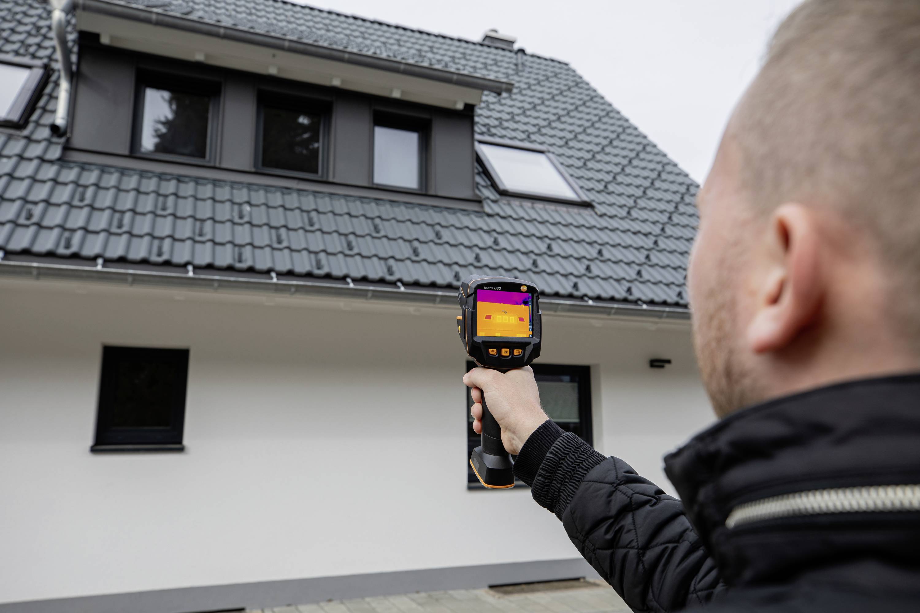 Een persoon houdt een warmtebeeldcamera en controleert de isolatie op een modern dakdak met dakramen.