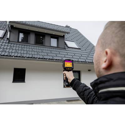 Een persoon houdt een warmtebeeldcamera en controleert de isolatie op een modern dakdak met dakramen.