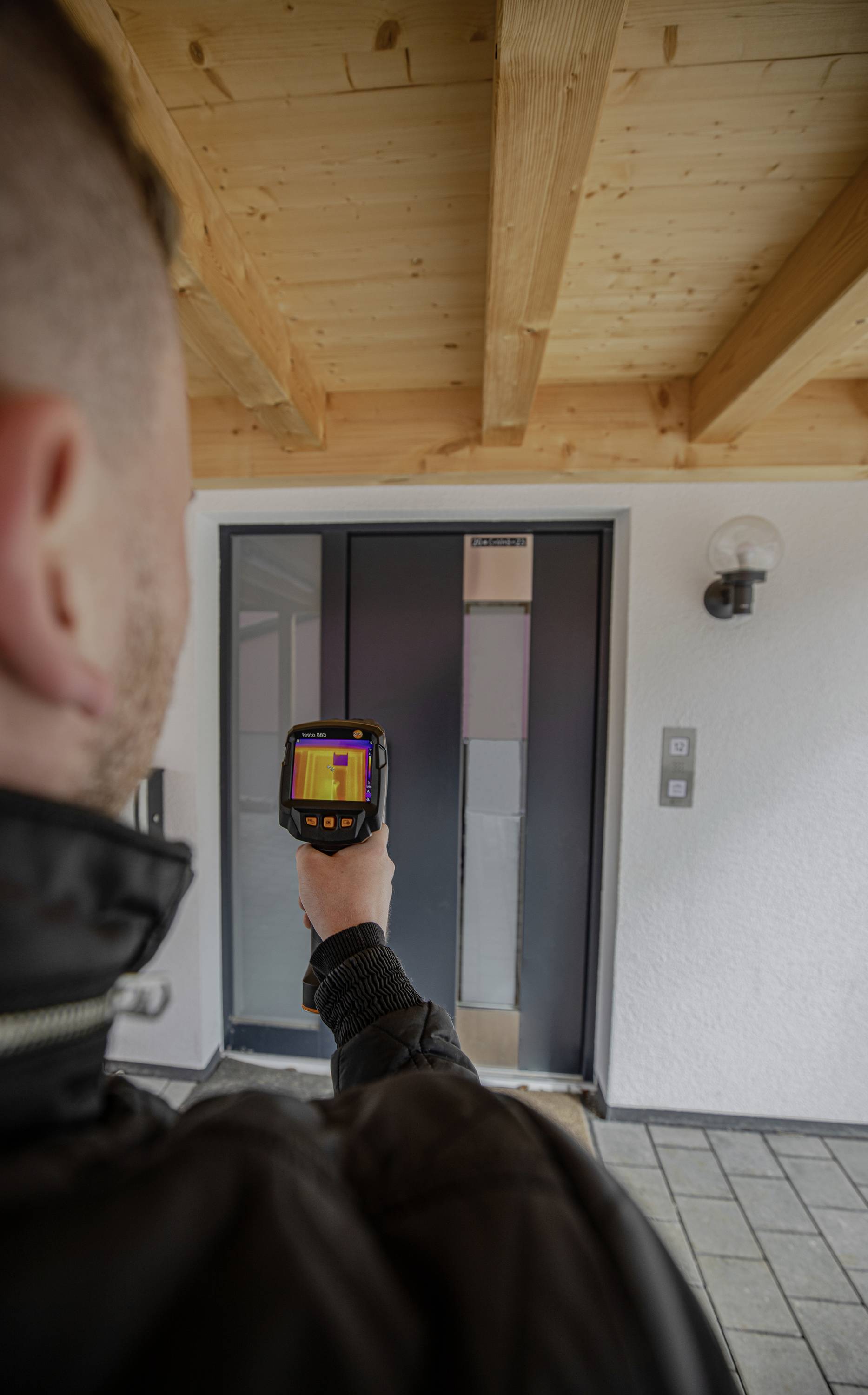 Een persoon gebruikt een warmtebeeldcamera om de voordeur te controleren op warmteverlies. De camera toont kleurveranderingen.