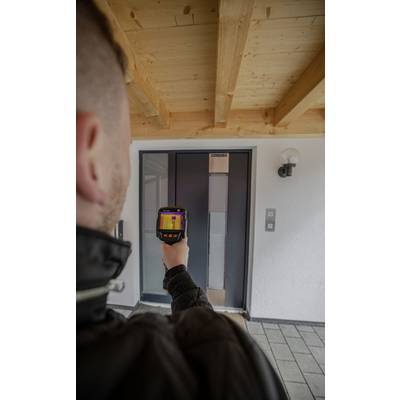 Een persoon gebruikt een warmtebeeldcamera om de voordeur te controleren op warmteverlies. De camera toont kleurveranderingen.