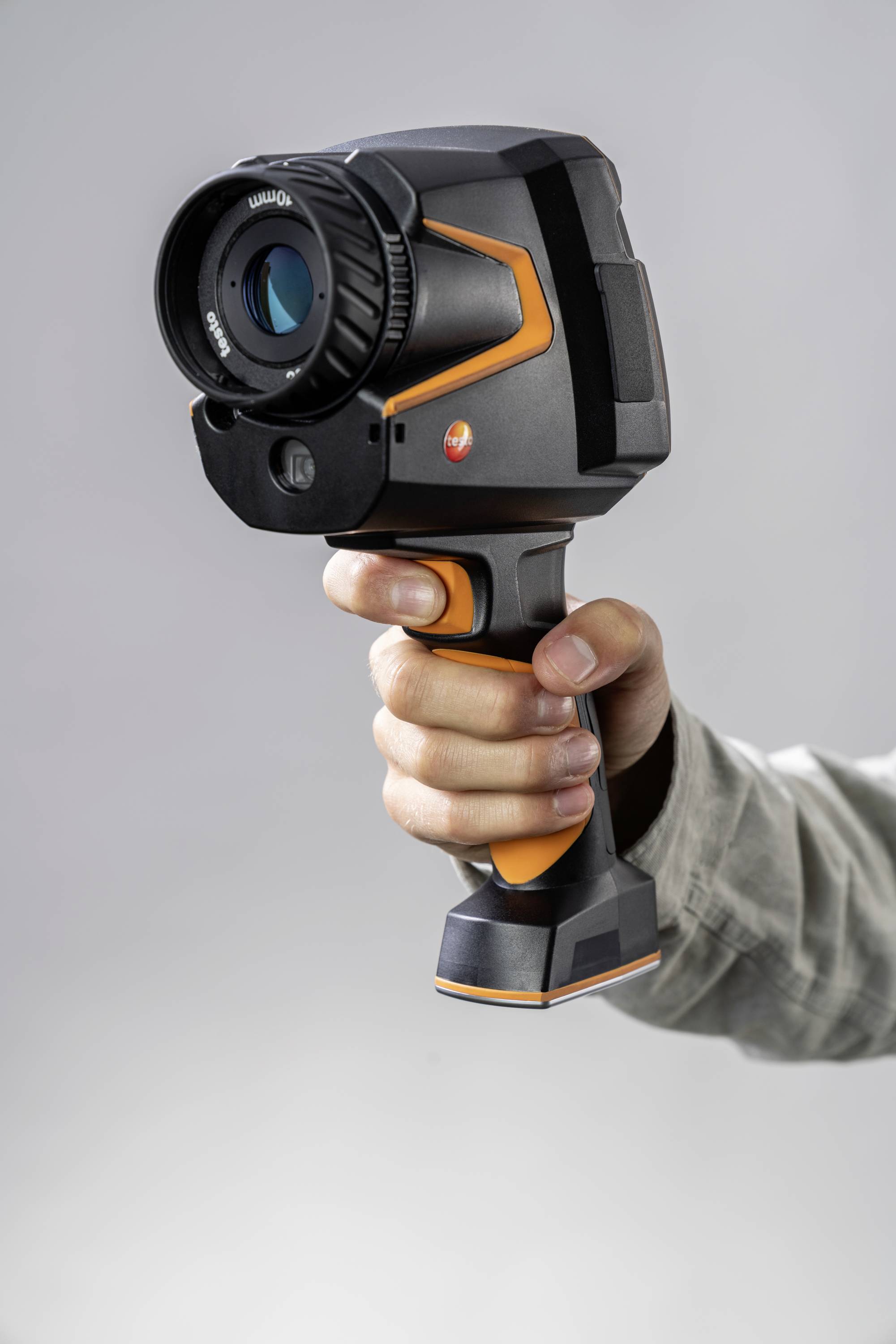 Een hand houdt een infraroodcamera vast, gericht op een grijze achtergrond.