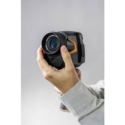 Een persoon houdt een warmtebeeldcamera tegen een grijze achtergrond. De camera heeft een groot objectief en oranje accenten.