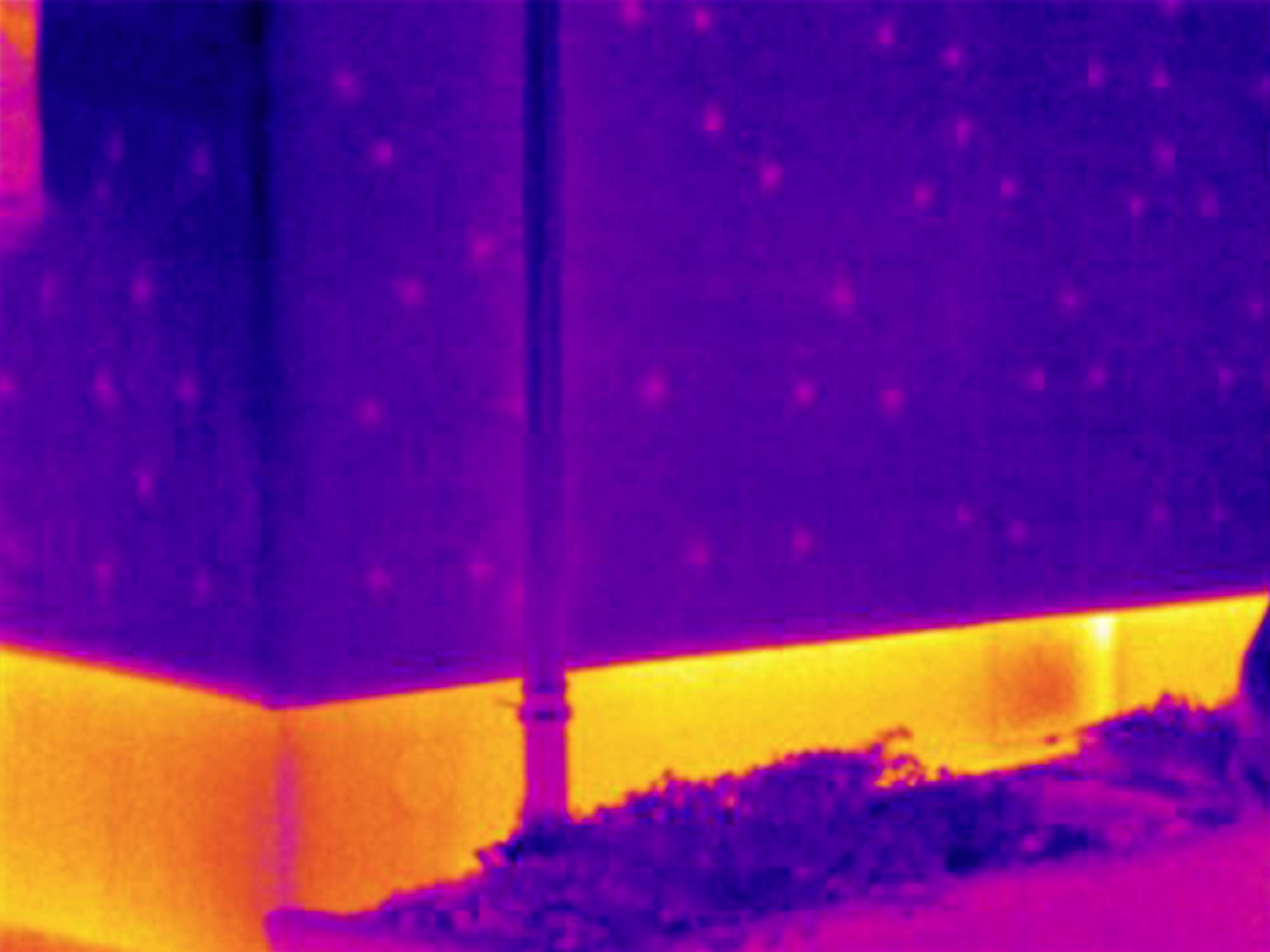 Warmtebeeldopname van een gebouwhoek. De basis toont intensieve warmtestraling in geel; bovenste gedeelten tonen minder warmte in paars.