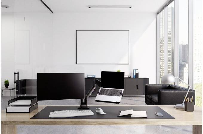 Modern, licht kantoor met een groot bureau, twee monitors en laptops. Op de achtergrond ramen met zicht op de stad.