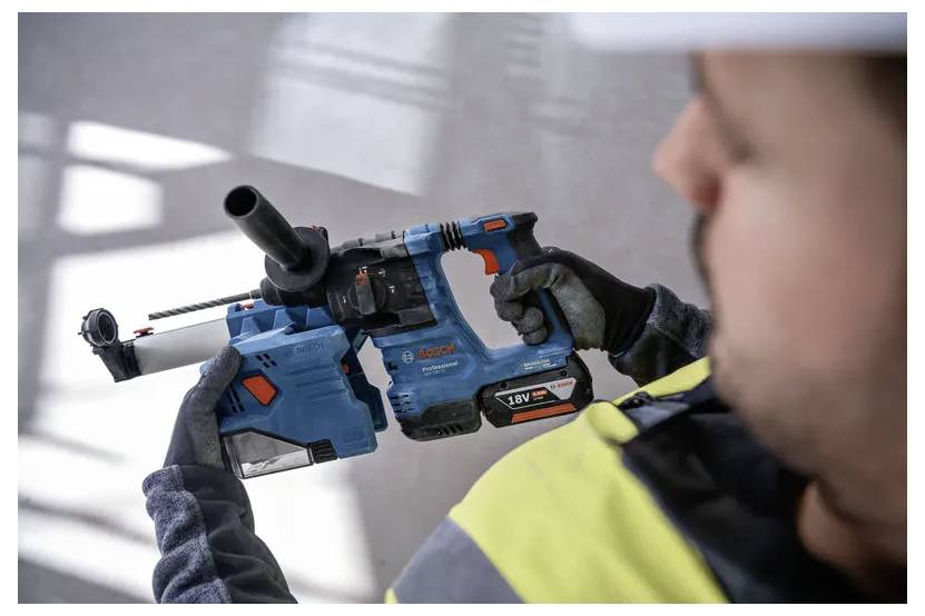 Een bouwvakker houdt een blauwe en zwarte accuboormachine vast, met de nadruk op zijn kenmerken, inclusief een stofafzuigingsaansluiting.